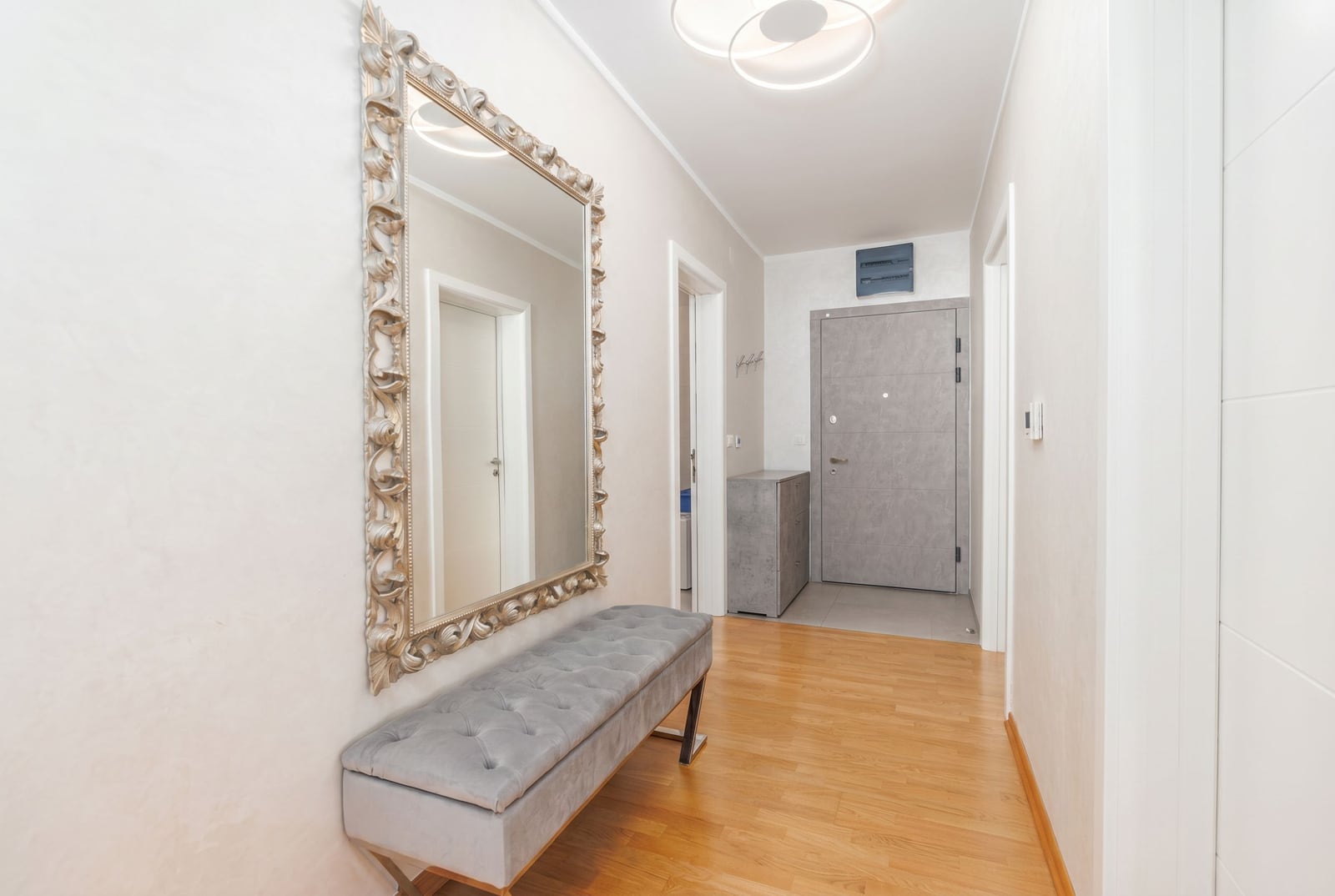 Bright hallway in a penthouse in Bečići, Montenegro: mirror in a carved frame, upholstered bench, and modern finishes.