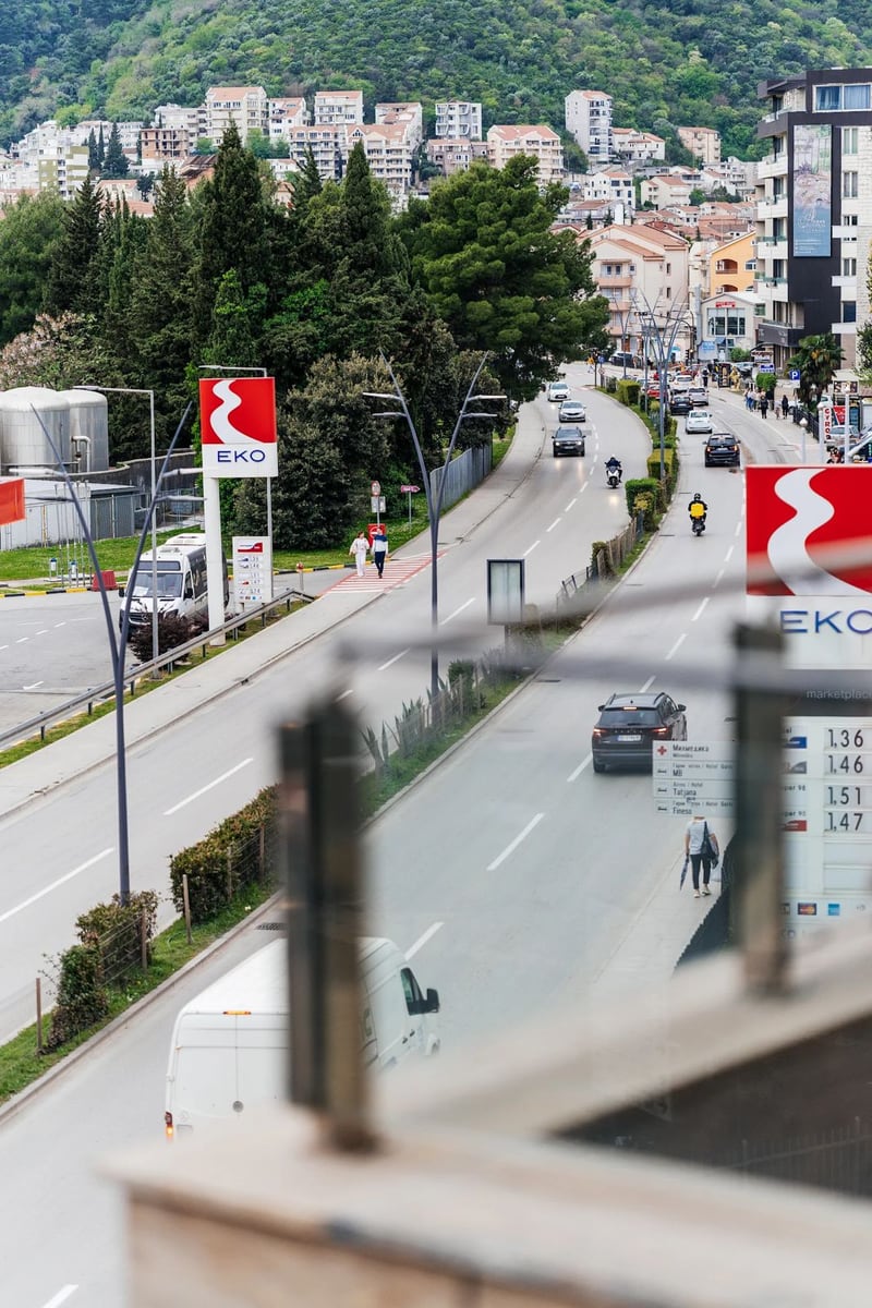 View from the apartment balcony in Budva, Montenegro: a city street, an EKO gas station, and a mountain landscape in the background.