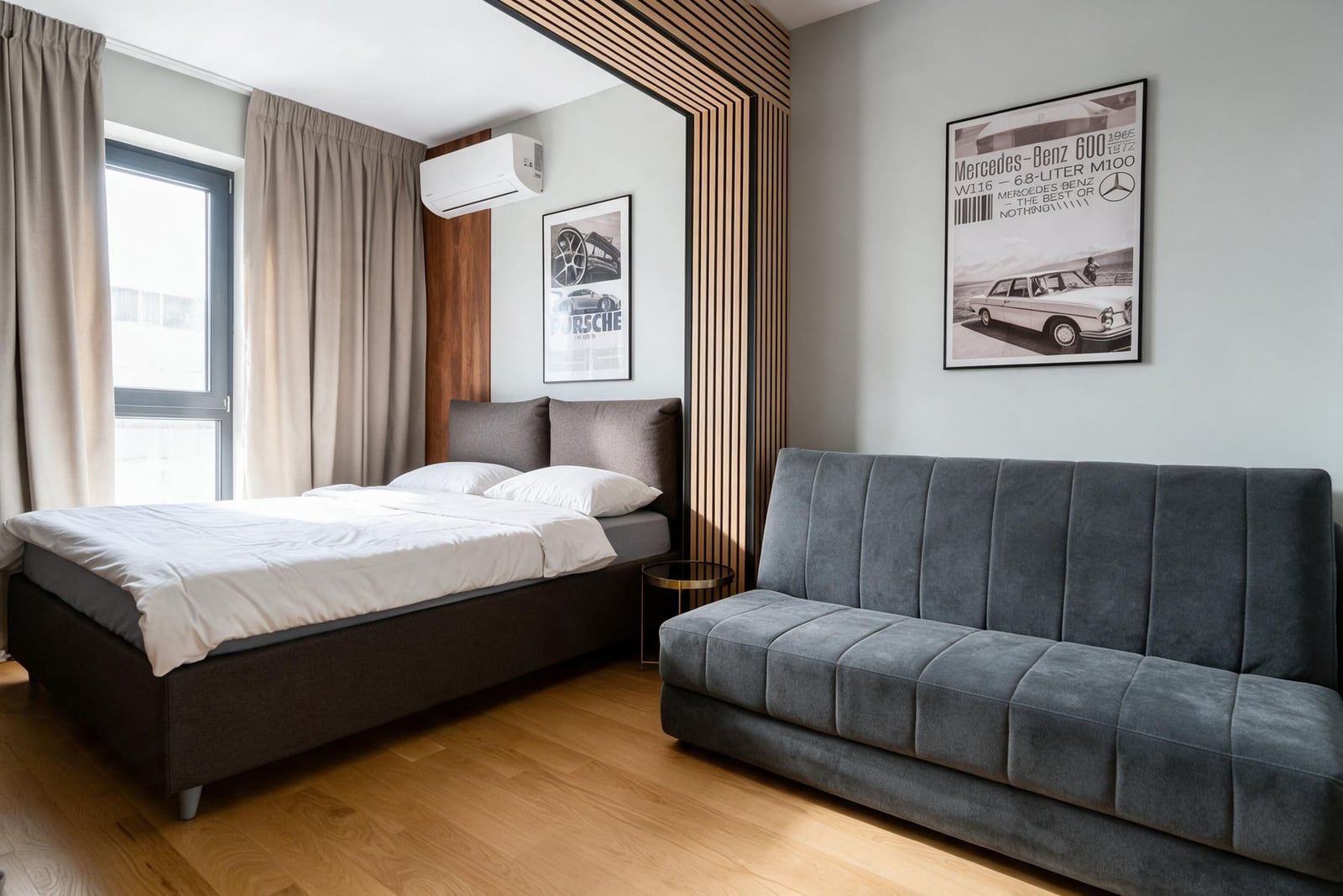 Modern bedroom featuring a double bed, grey sofa, wooden slat arch, and automotive wall art.