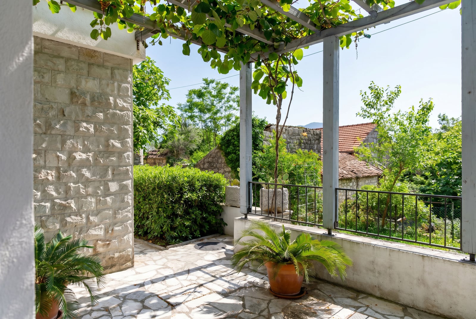 Cozy terrace with stone finish and pergola in an apartment in Risan, Montenegro, view of the green garden and historic houses.