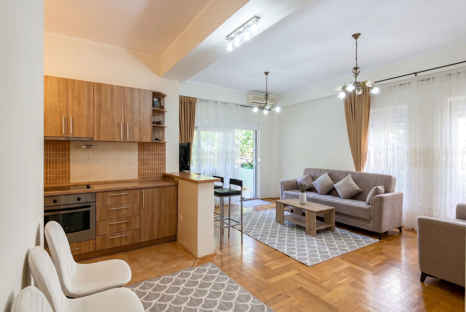 Modern living room with a kitchen in a Budva apartment, Montenegro: wooden cabinetry, a plush sofa, and access to a terrace.