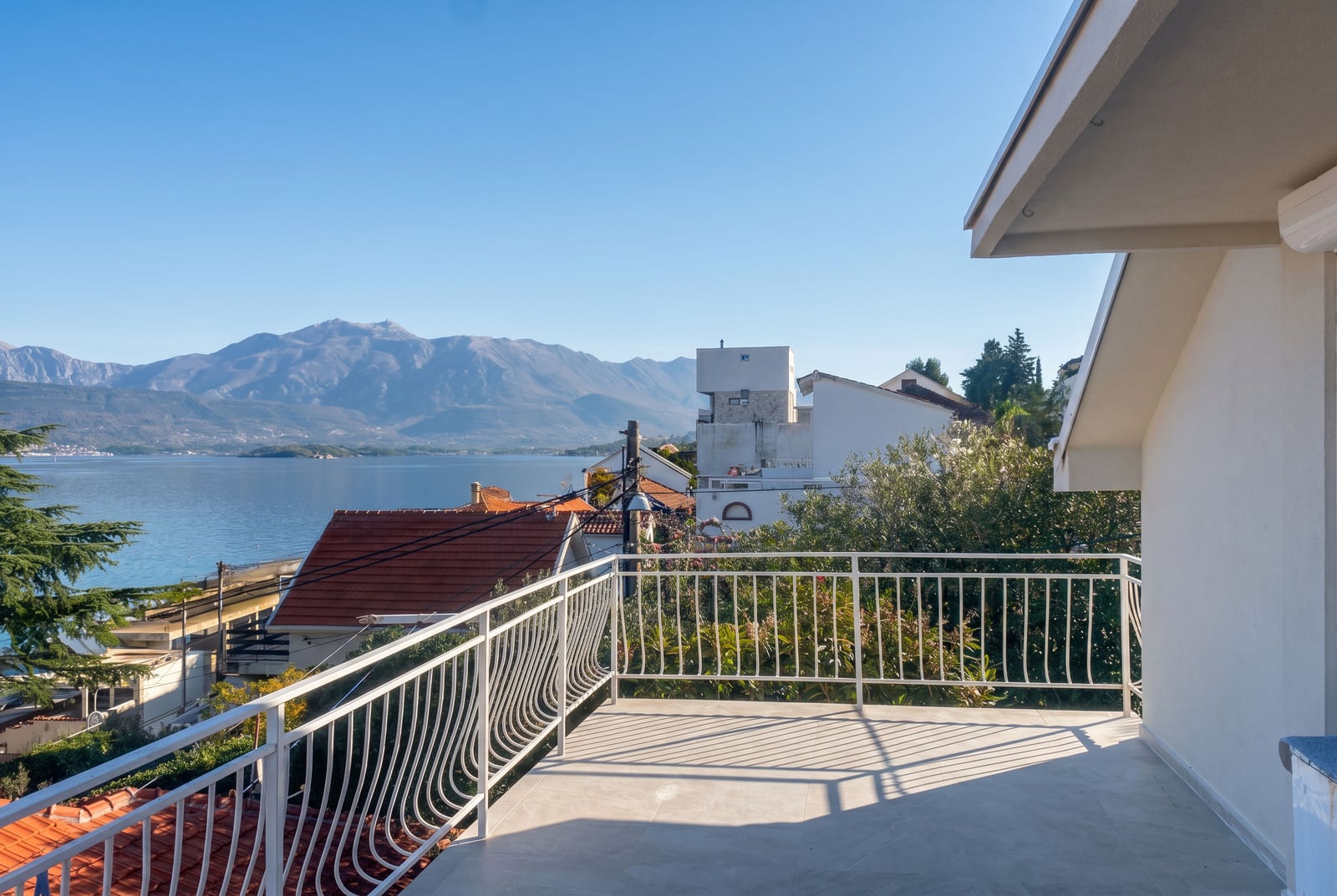 Spacious terrace of a house in Krašići, Montenegro, with a panoramic view of the sea and mountains, light-toned finishes, and white railings.