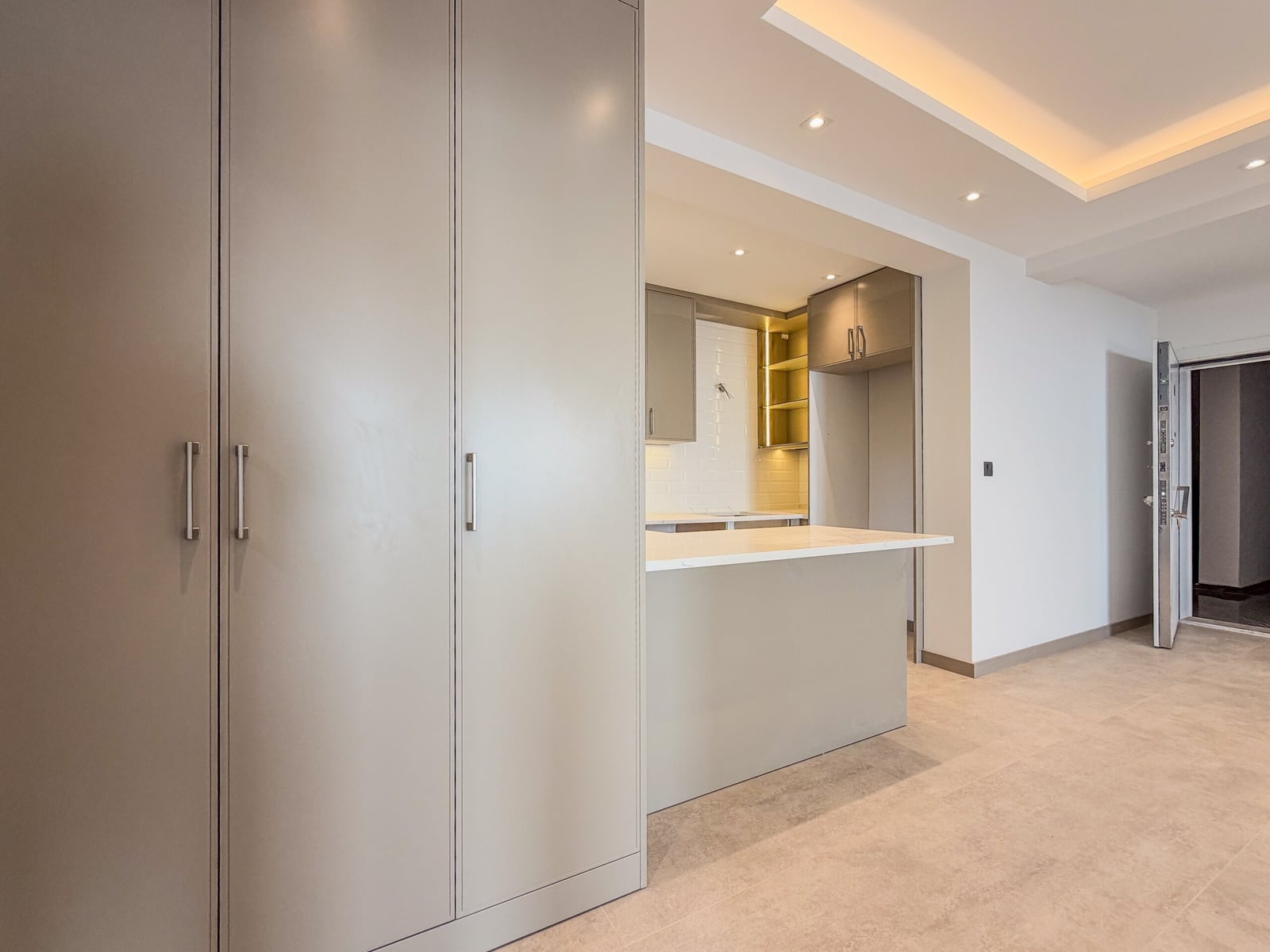 Modern kitchen featuring tall grey cabinets, a white stone island counter, and visible cooking area in the background.