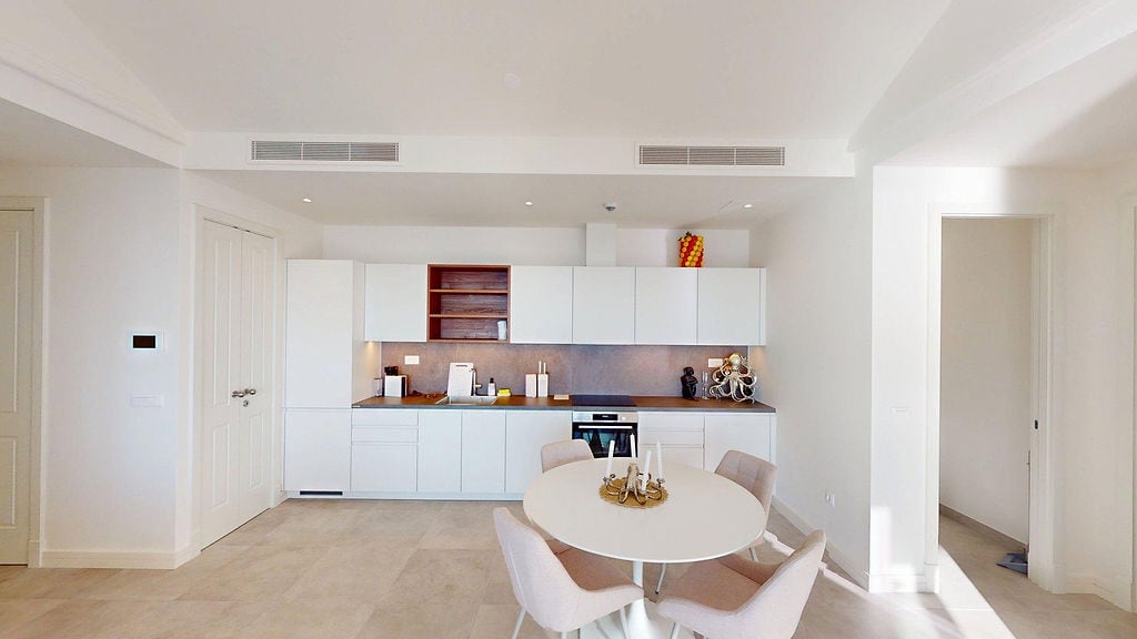 Modern white kitchen with dining area in a Lustica Bay apartment, Montenegro: built-in appliances and light design.