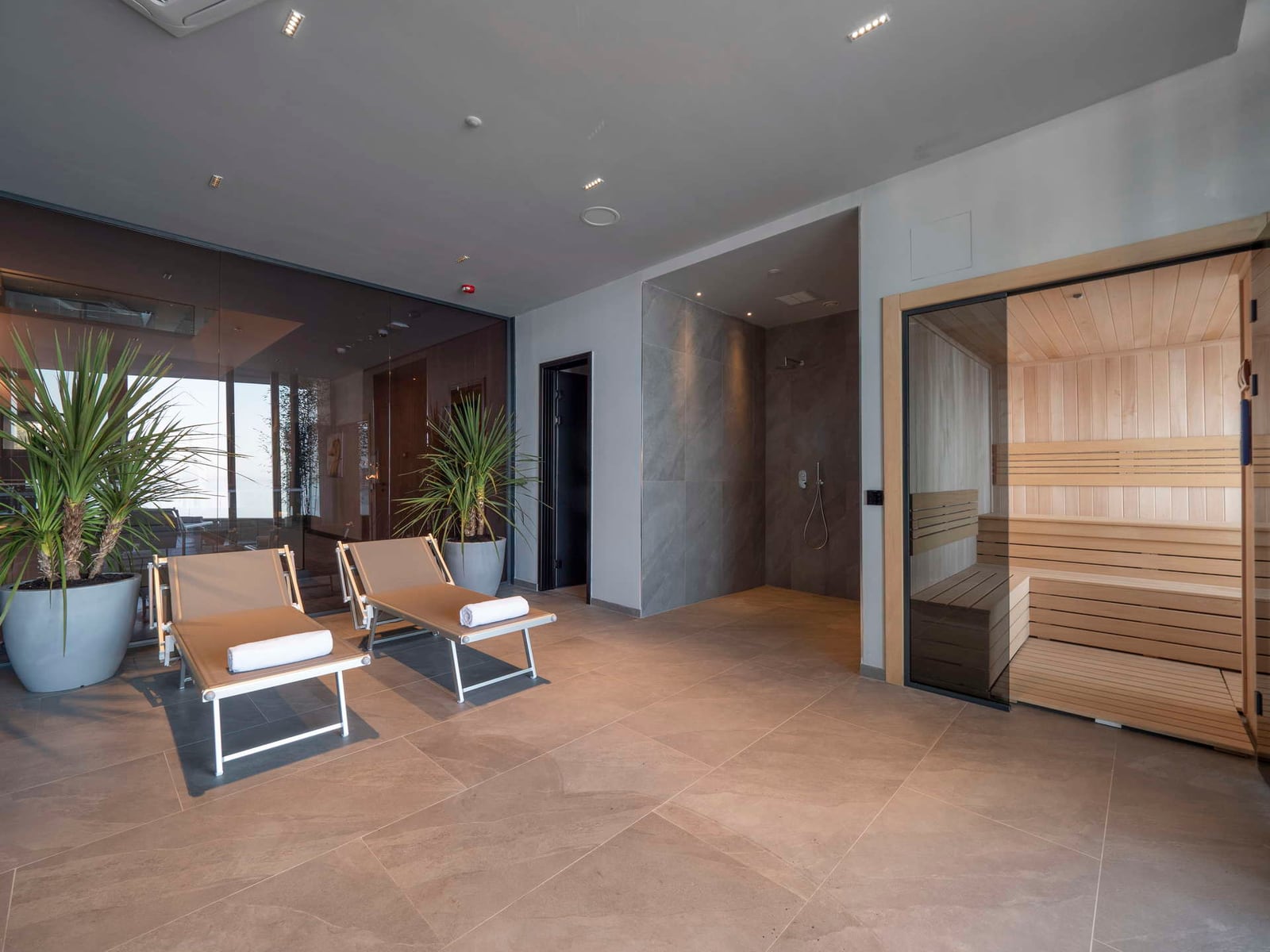 Relaxation room featuring lounge chairs, a wooden sauna, and an open shower area with tiled floors.