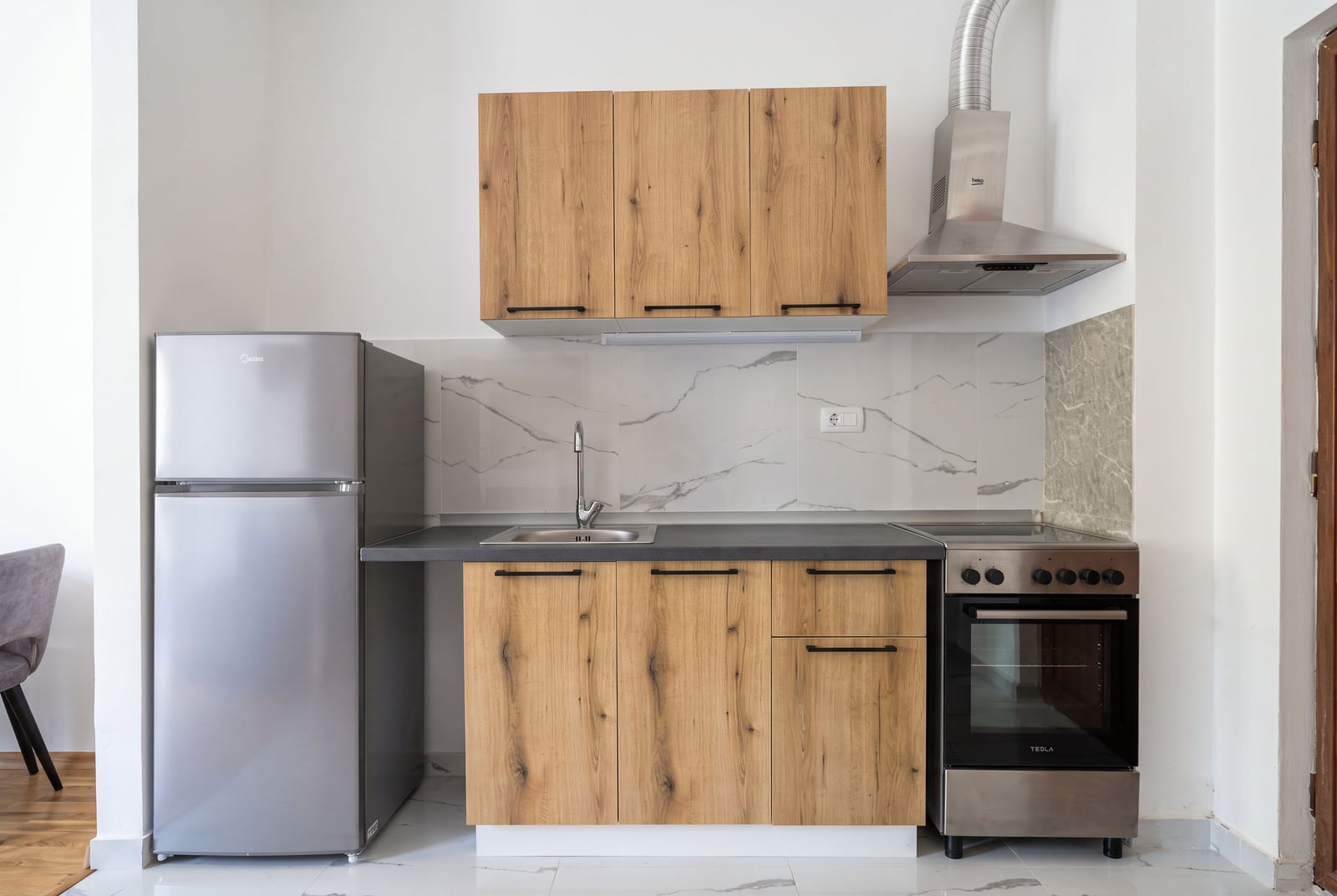 Modern kitchen with wooden facades, appliances, and a marble backsplash in an apartment in Budva, Montenegro.