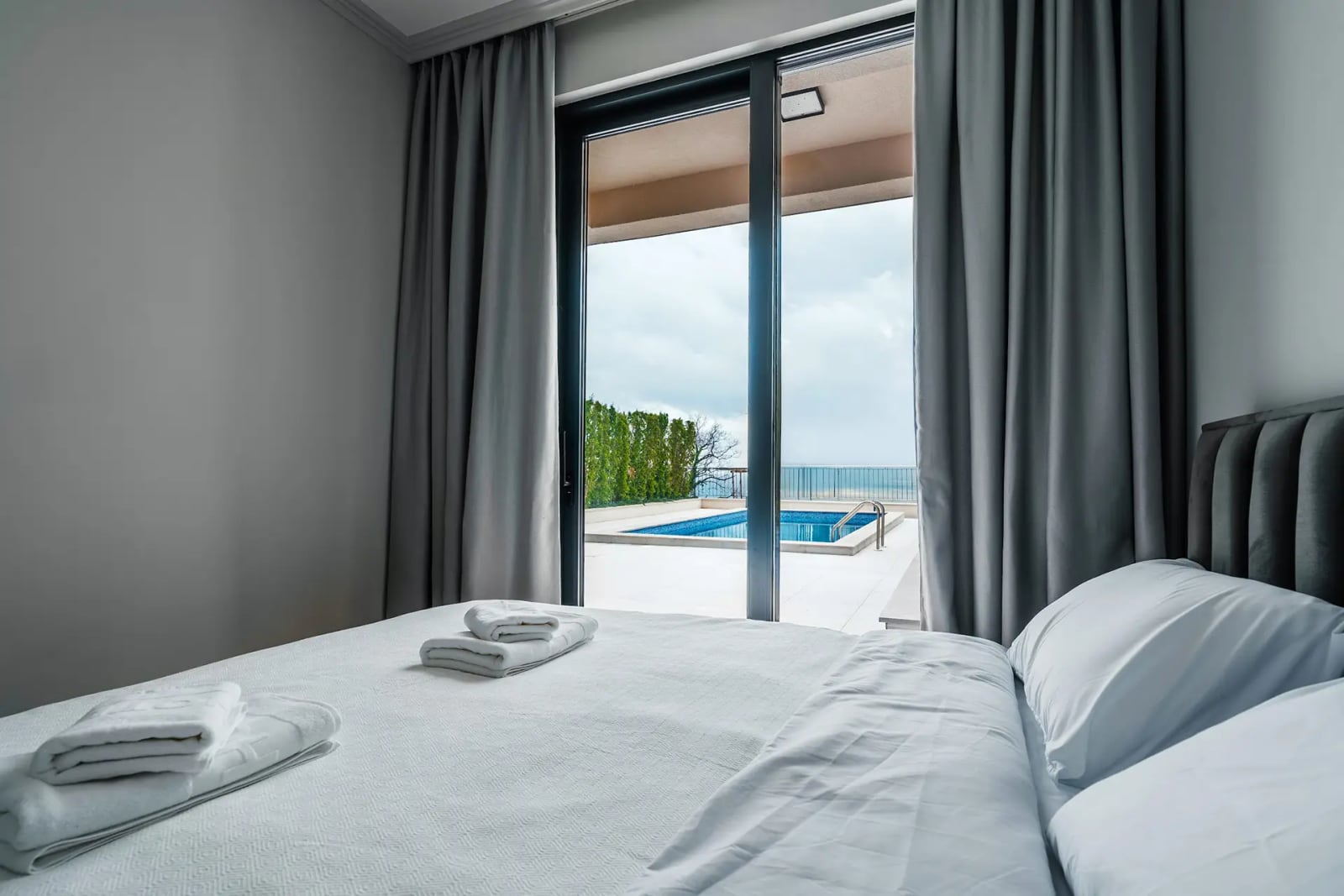 Bedroom in a villa in Reževići, Montenegro: panoramic view of the terrace with a pool and the sea through a glass door.