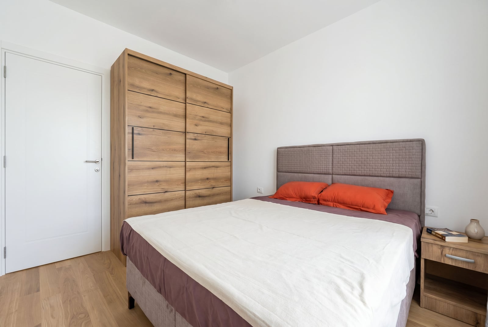 Bedroom in an apartment in Bečići, Montenegro: double bed, wooden sliding-door wardrobe, and a modern-style nightstand.