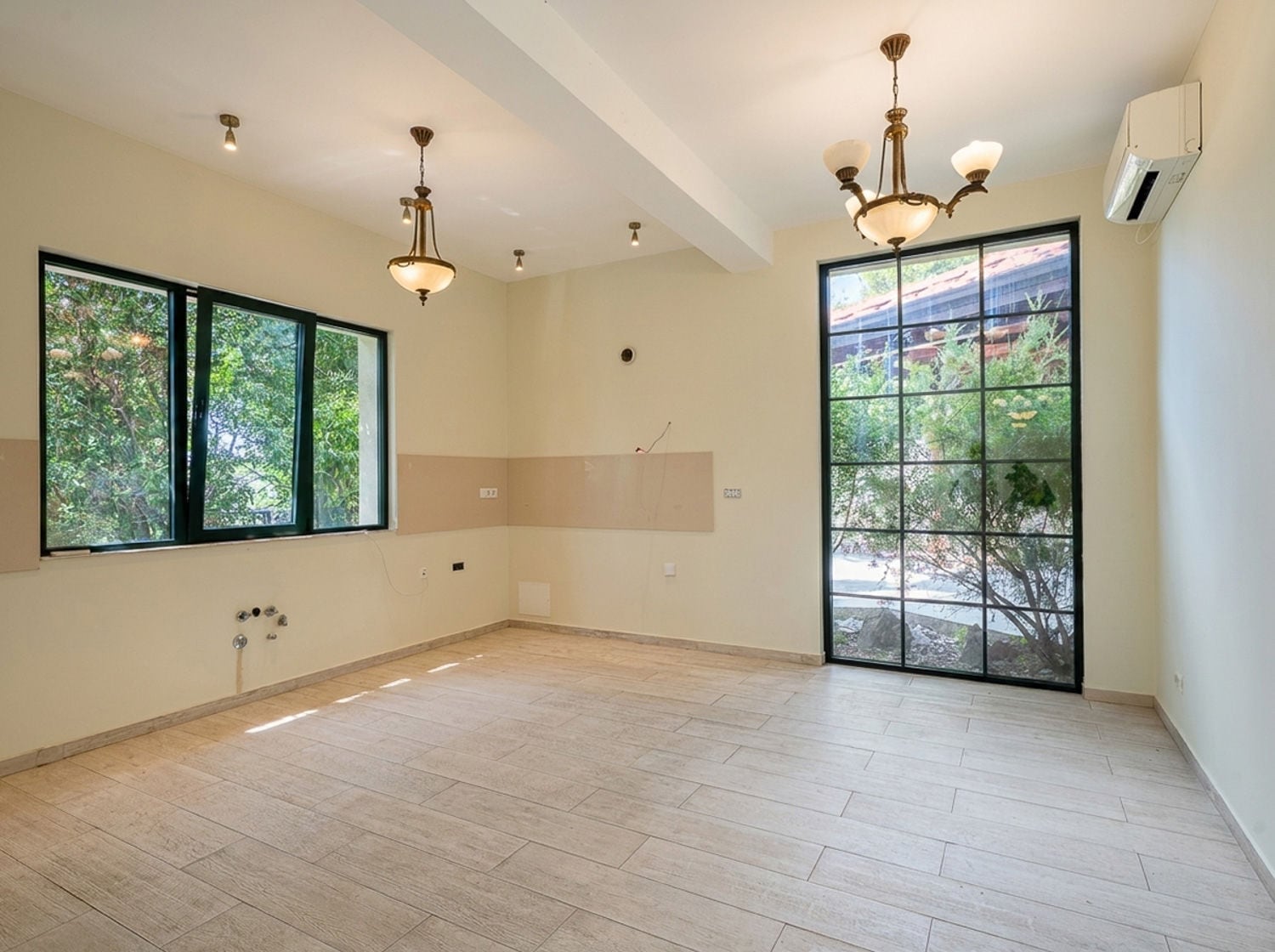 Empty room with tile flooring, pendant lights, and visible water pipes near the floor indicating a kitchen setup.
