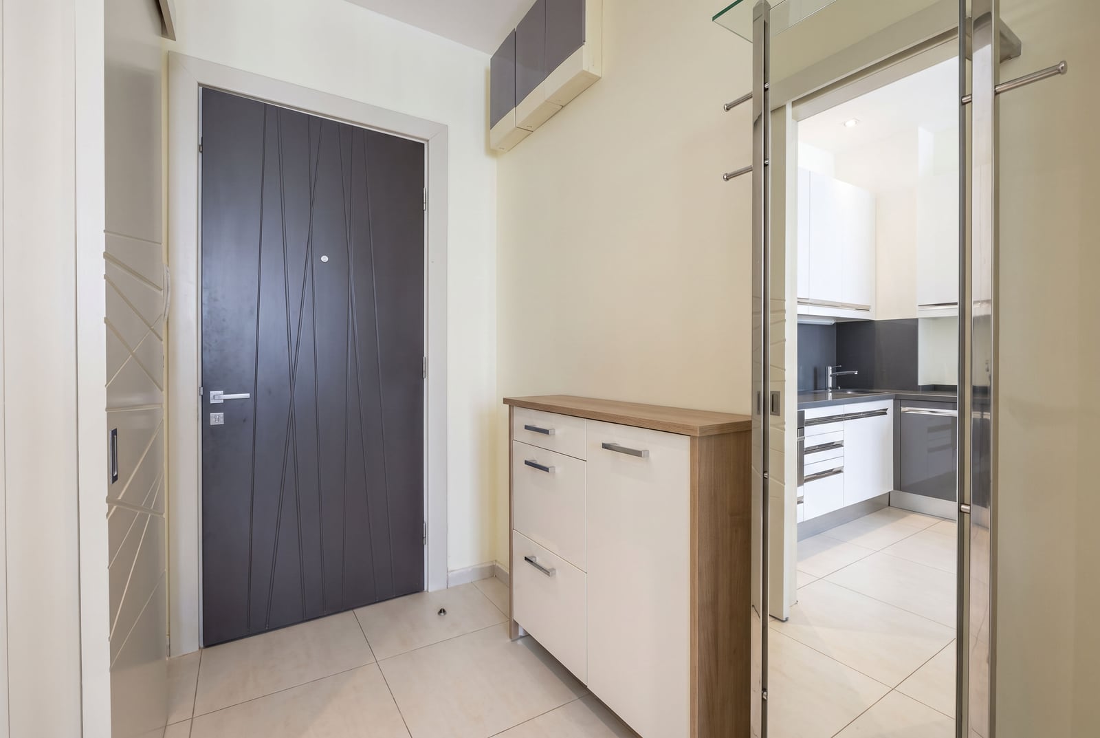 Entryway with a dark grey door, white storage cabinet, and a view into the kitchen through a glass partition.