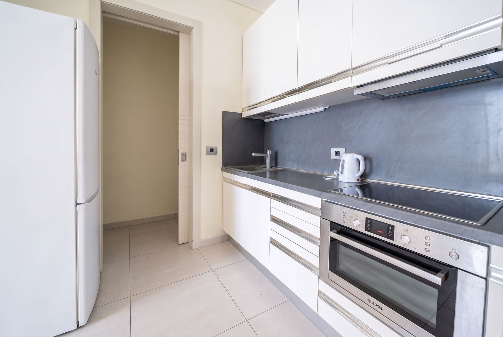 Modern kitchen featuring white cabinets, grey countertop, built-in Bosch oven, and a large refrigerator.