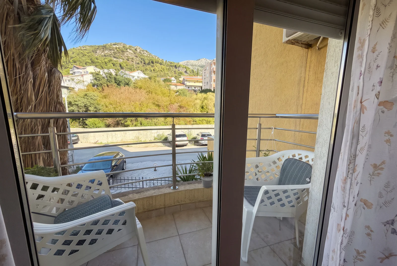 View of a balcony with white plastic chairs, metal railing, and a mountain landscape in the background.