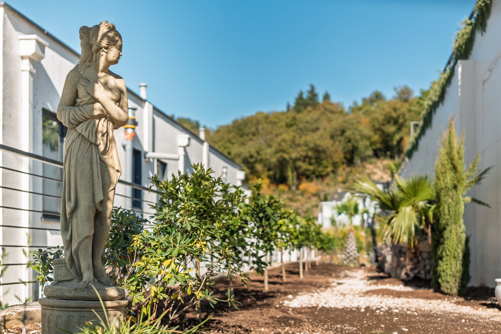 Antique statue in the landscaped garden of a townhouse in Kavač, Montenegro, with a view of green hills and a modern facade.