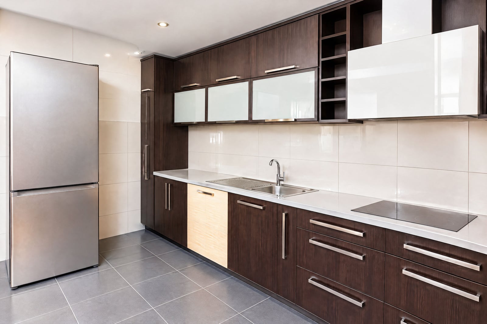 Modern kitchen featuring dark wood cabinetry, a stainless steel refrigerator, sink, and induction cooktop.