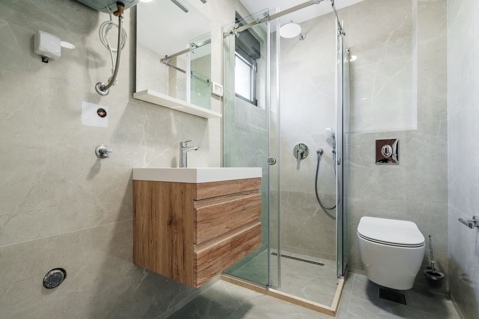 Modern bathroom in Budva residential complex, Montenegro: shower cabin, wood-look floating vanity, and light-colored tiles.