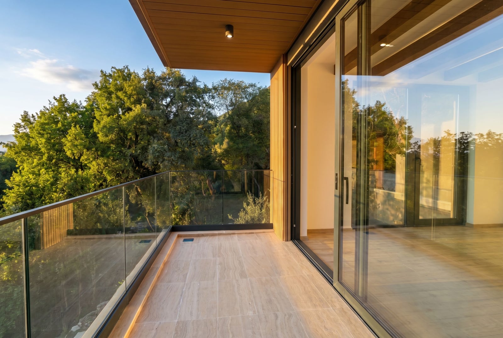 Modern villa balcony in Kavac, Montenegro, with panoramic glazing, stone flooring, and a view of the green forest.