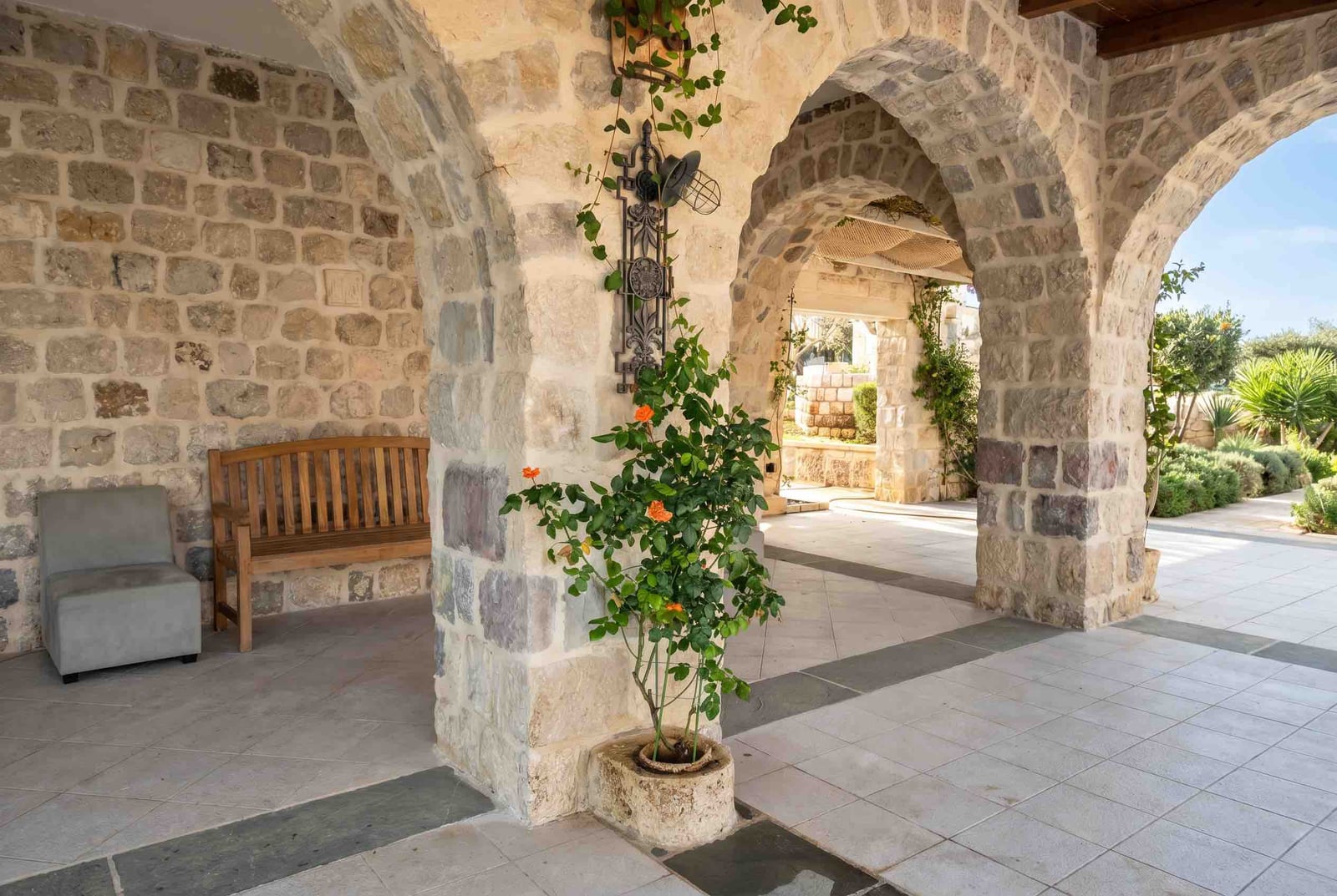 Covered terrace with stone arches and garden furniture in a house in Luštica, Montenegro. Cozy courtyard with plants.
