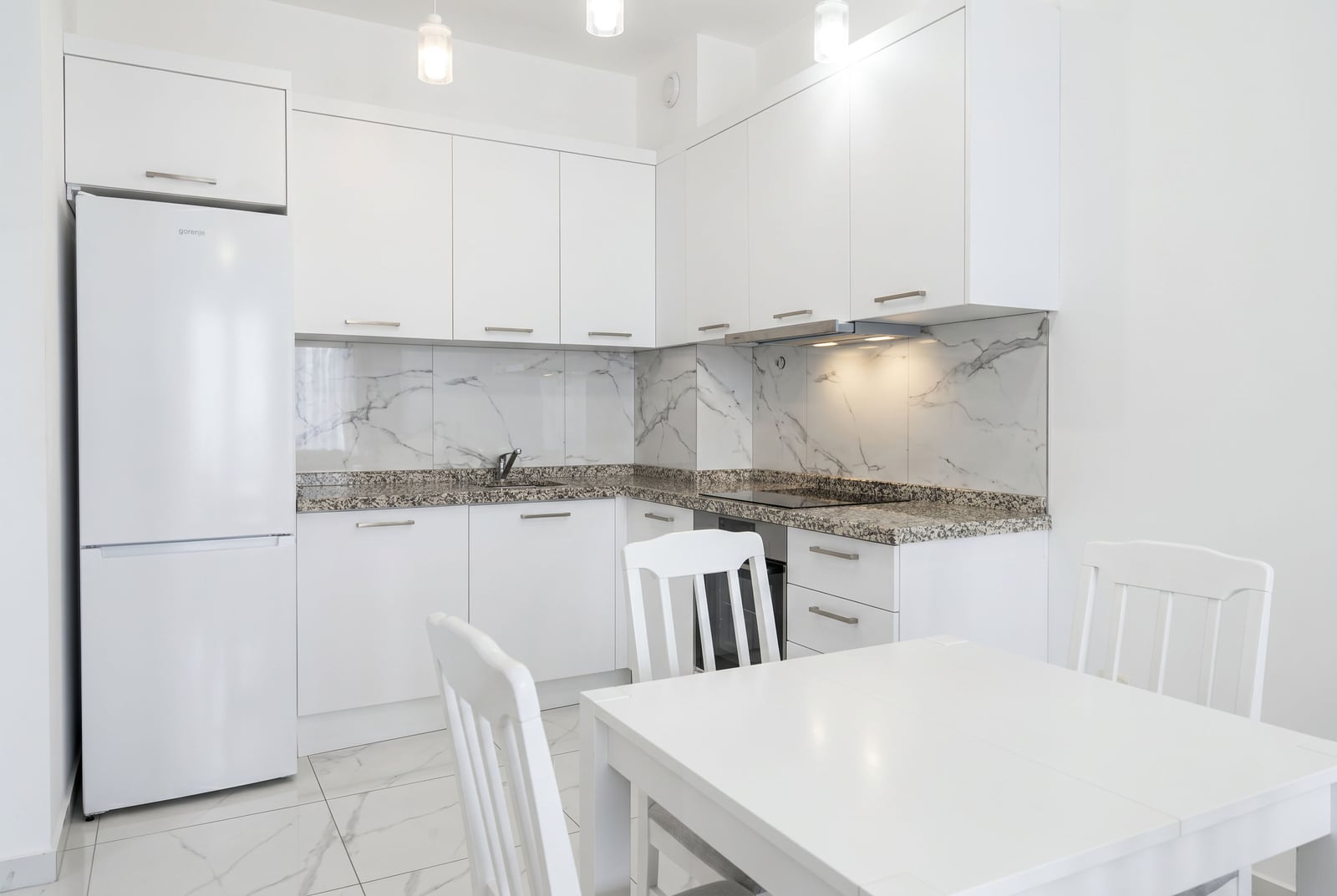 Modern white kitchen with furniture, appliances, and a dining area in an apartment in Budva, Montenegro.