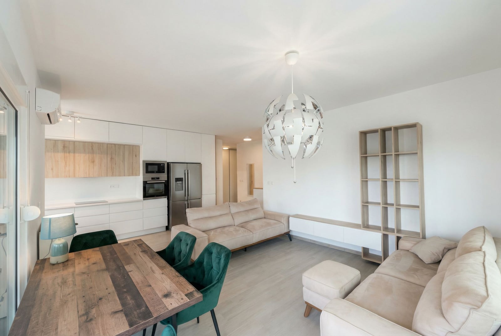 Modern living room with kitchen in an apartment, Becici, Montenegro: light furniture, dining area, and a designer chandelier.
