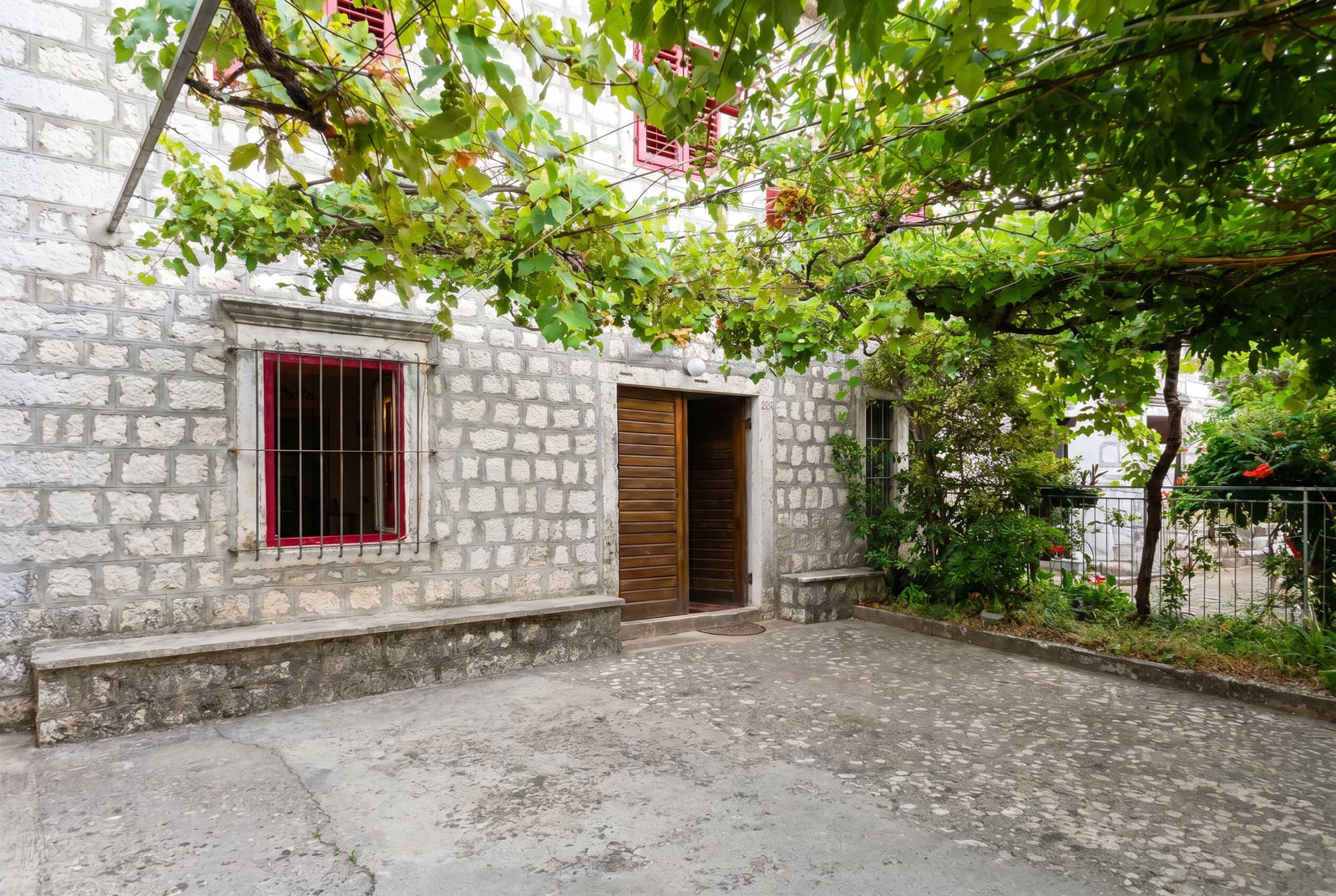 Stone house in Dobrota, Montenegro: natural stone facade, terrace with grapevines, and wooden front door.