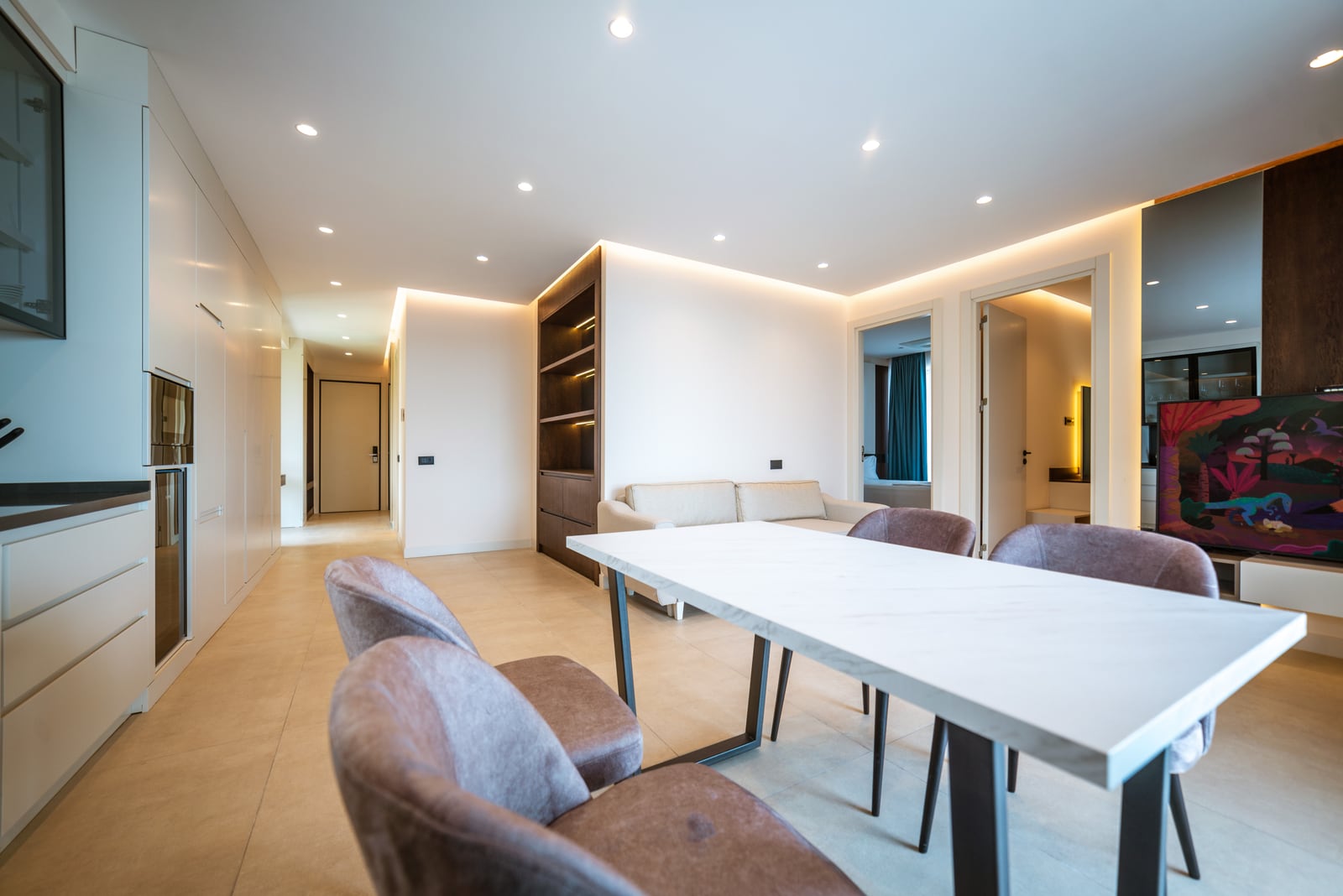 Modern living room with dining area in an apartment, Bečići, Montenegro: light furniture, built-in kitchen, and accent lighting.