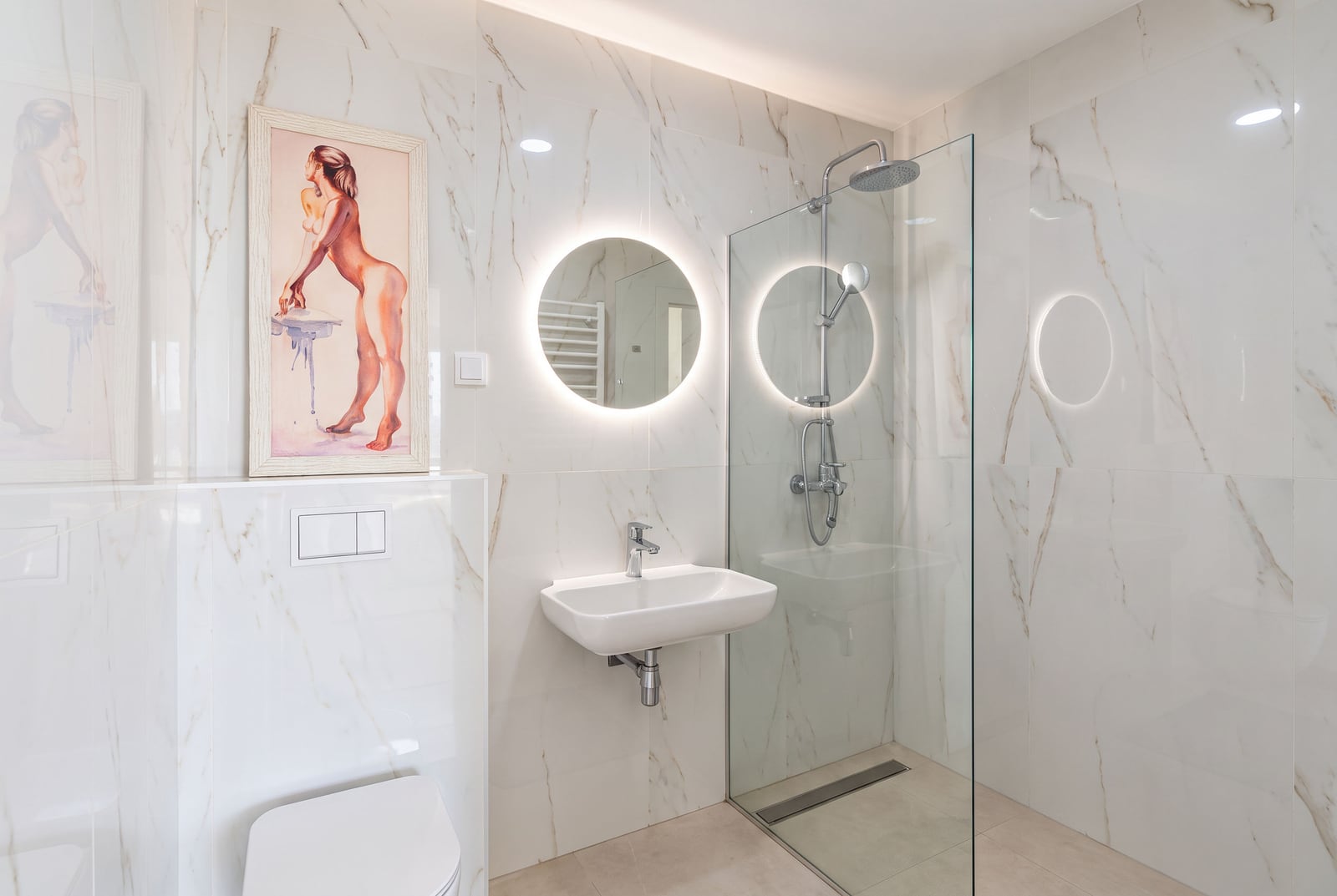 Modern bathroom with marble tiles, glass shower enclosure, wall-mounted sink, and round backlit mirror.