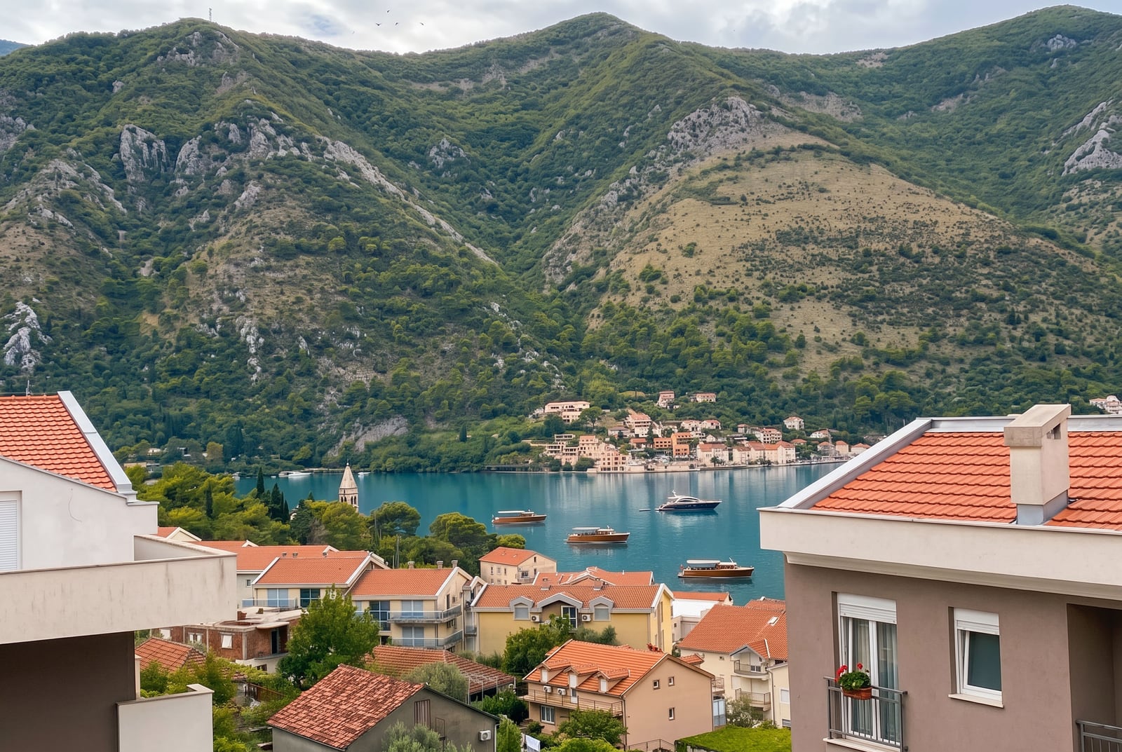 Panoramic view of the Bay of Kotor and mountains from an apartment in Dobrota, Montenegro: tiled roofs and yachts on the water.