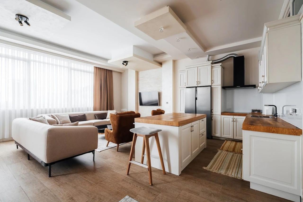 Modern living room with an island kitchen in an apartment in Budva, Montenegro: light furniture, wooden countertop, panorama.