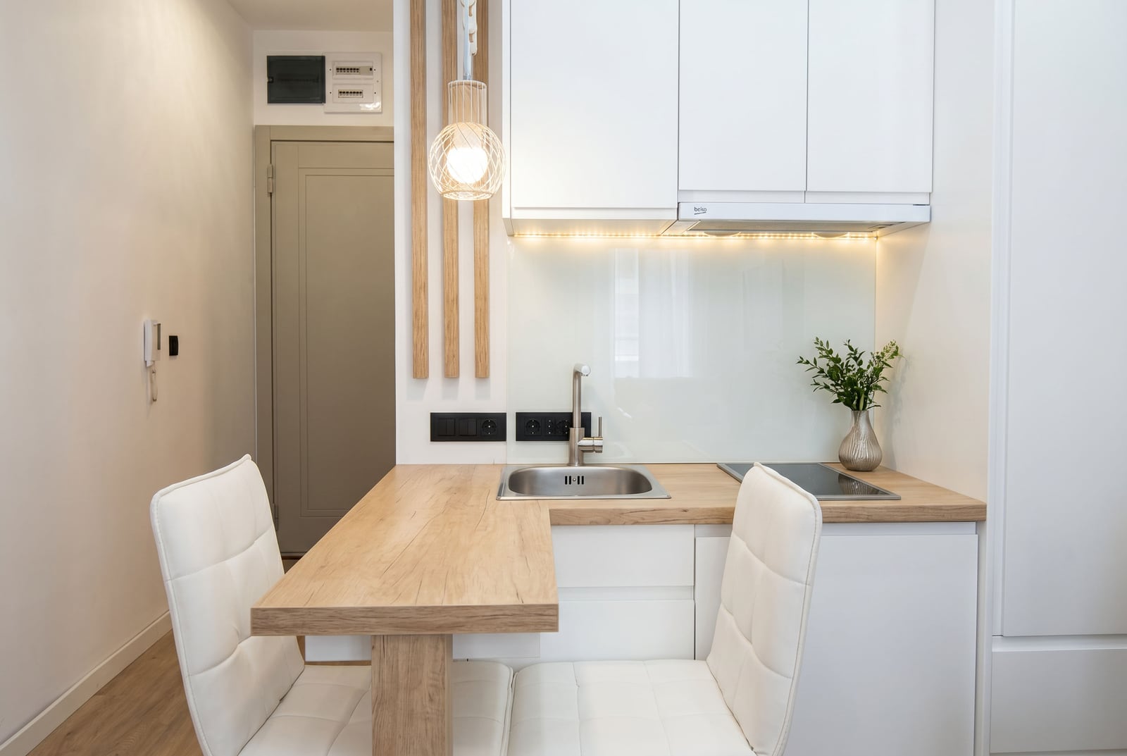 Modern kitchen in an apartment, Becici, Montenegro: white cabinets, wooden breakfast bar, and stylish lighting.