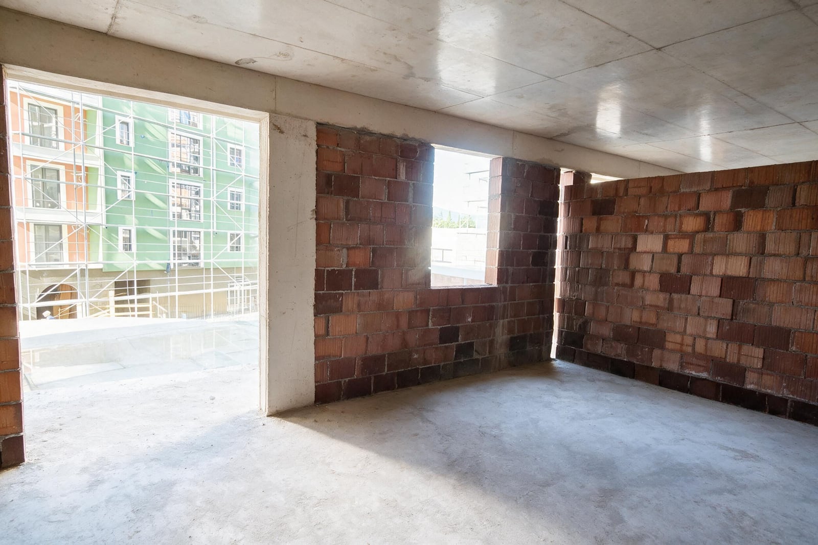 Unfinished room with exposed brick walls and concrete floor, construction scaffolding visible through the opening.