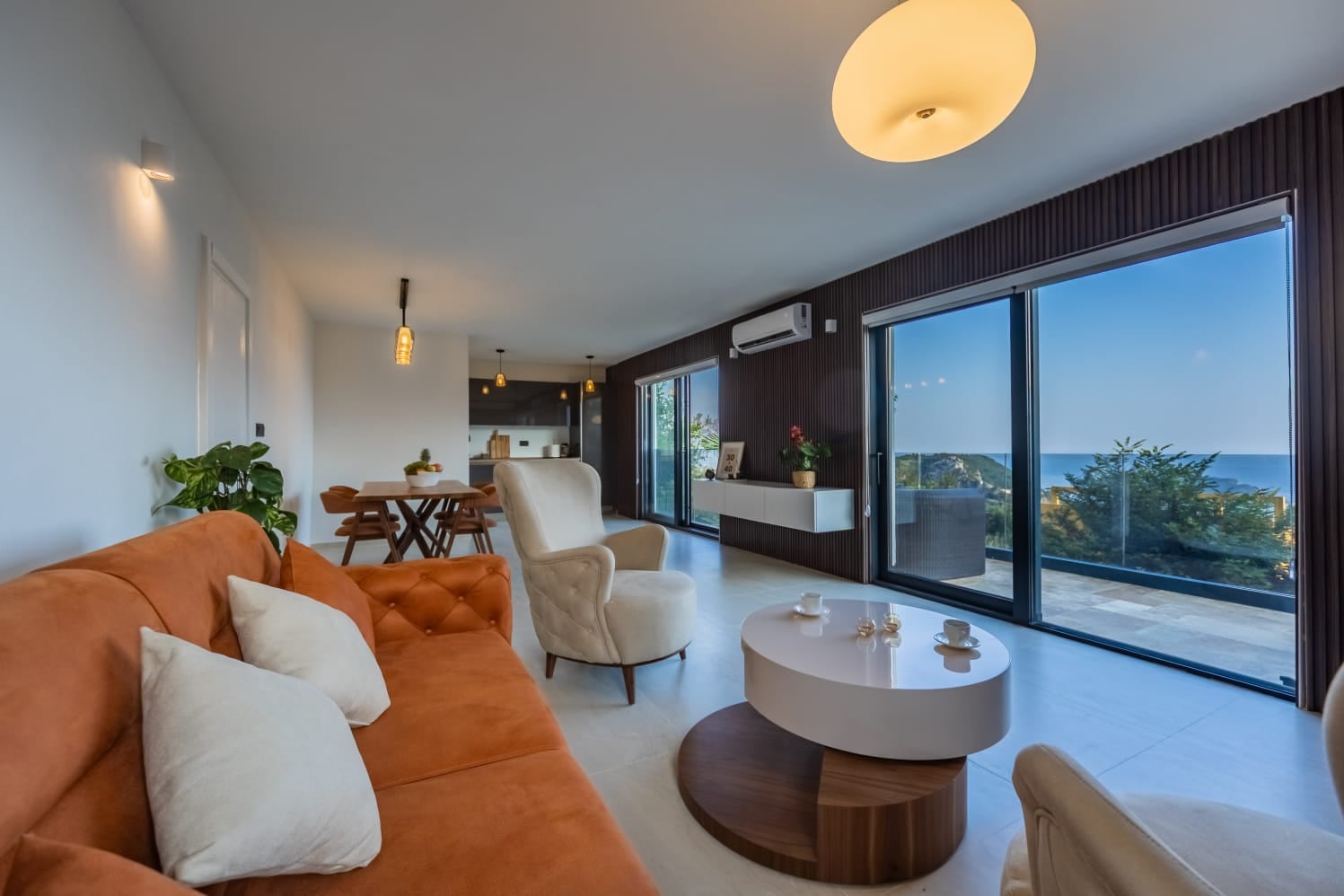 Modern living room in a villa in Budva, Montenegro: orange sofa, panoramic windows with sea view, and terrace.