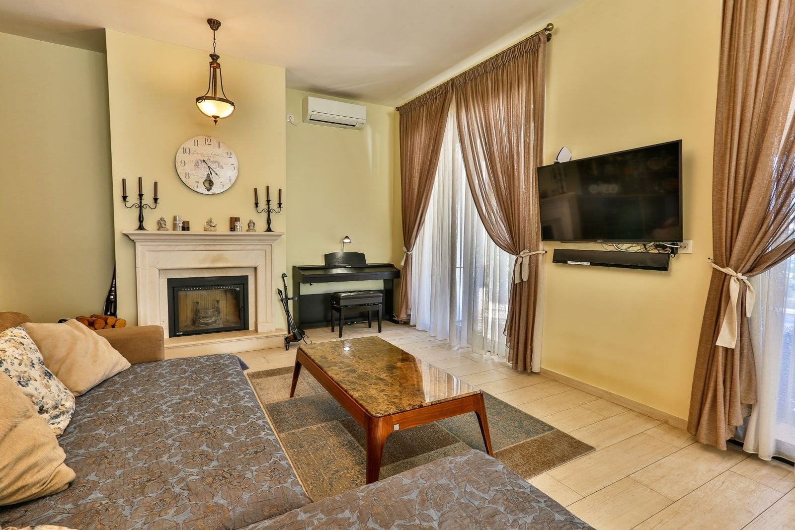 Living room with a fireplace, piano, and TV in the interior of a villa in Tivat, Montenegro. Cozy lounge area with upholstered furniture.