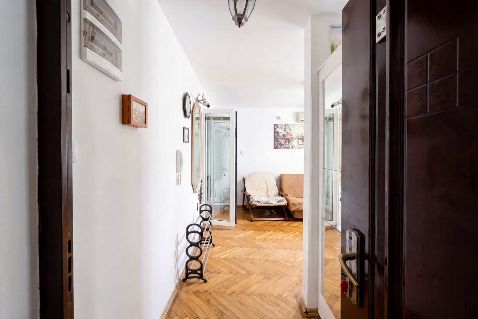 Entryway with parquet floor, shoe rack, and mirror; living room with chair visible ahead.