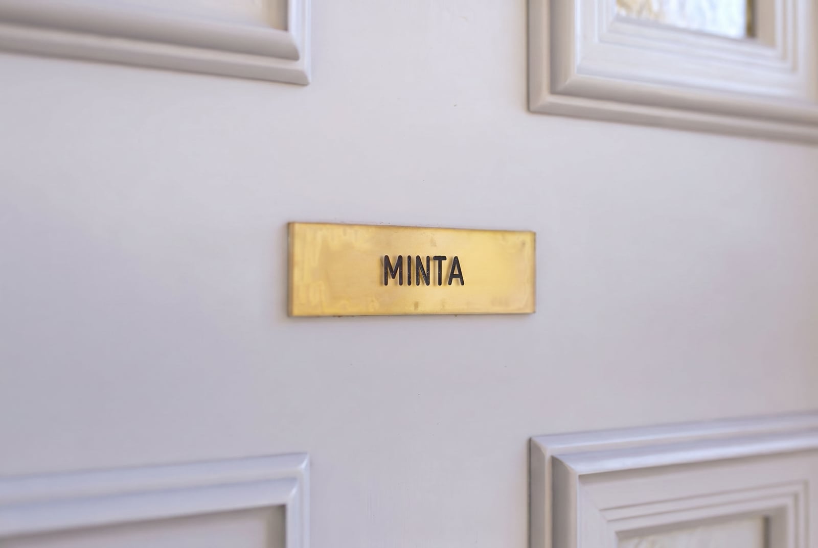 Gold plaque with the inscription "Minta" on a white paneled door of an apartment in the town of Risan, Montenegro.