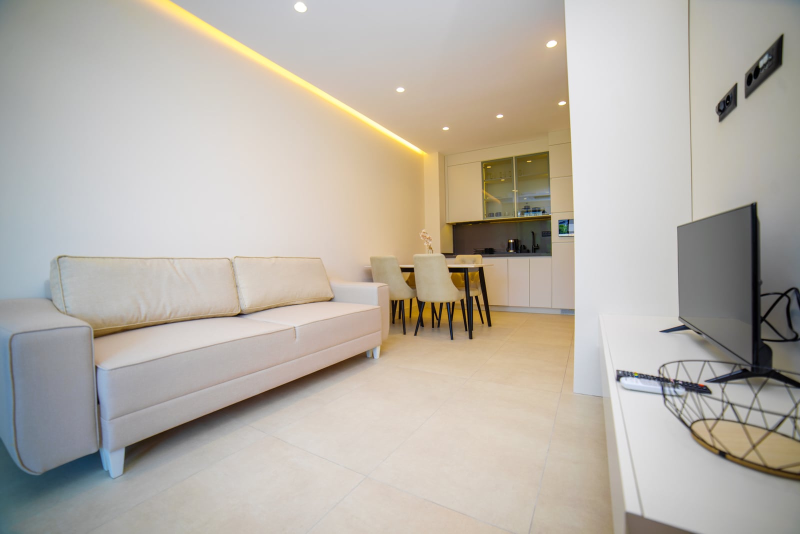 Modern living room with kitchen in an apartment in Bečići, Montenegro: light-colored sofa, dining area, and built-in furniture.