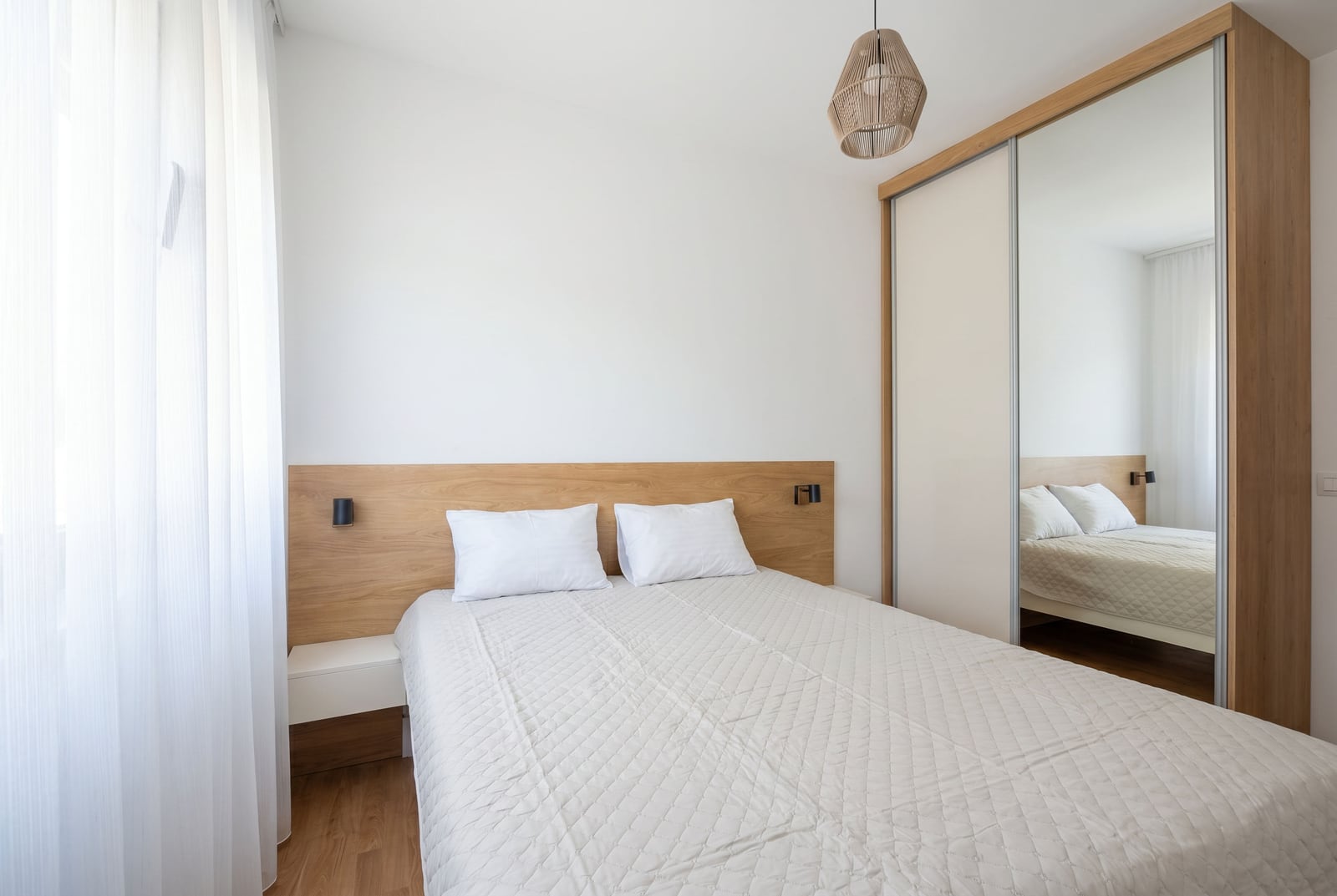 Modern bedroom in a Budva apartment, Montenegro: double bed, wooden headboard, and mirrored wardrobe.