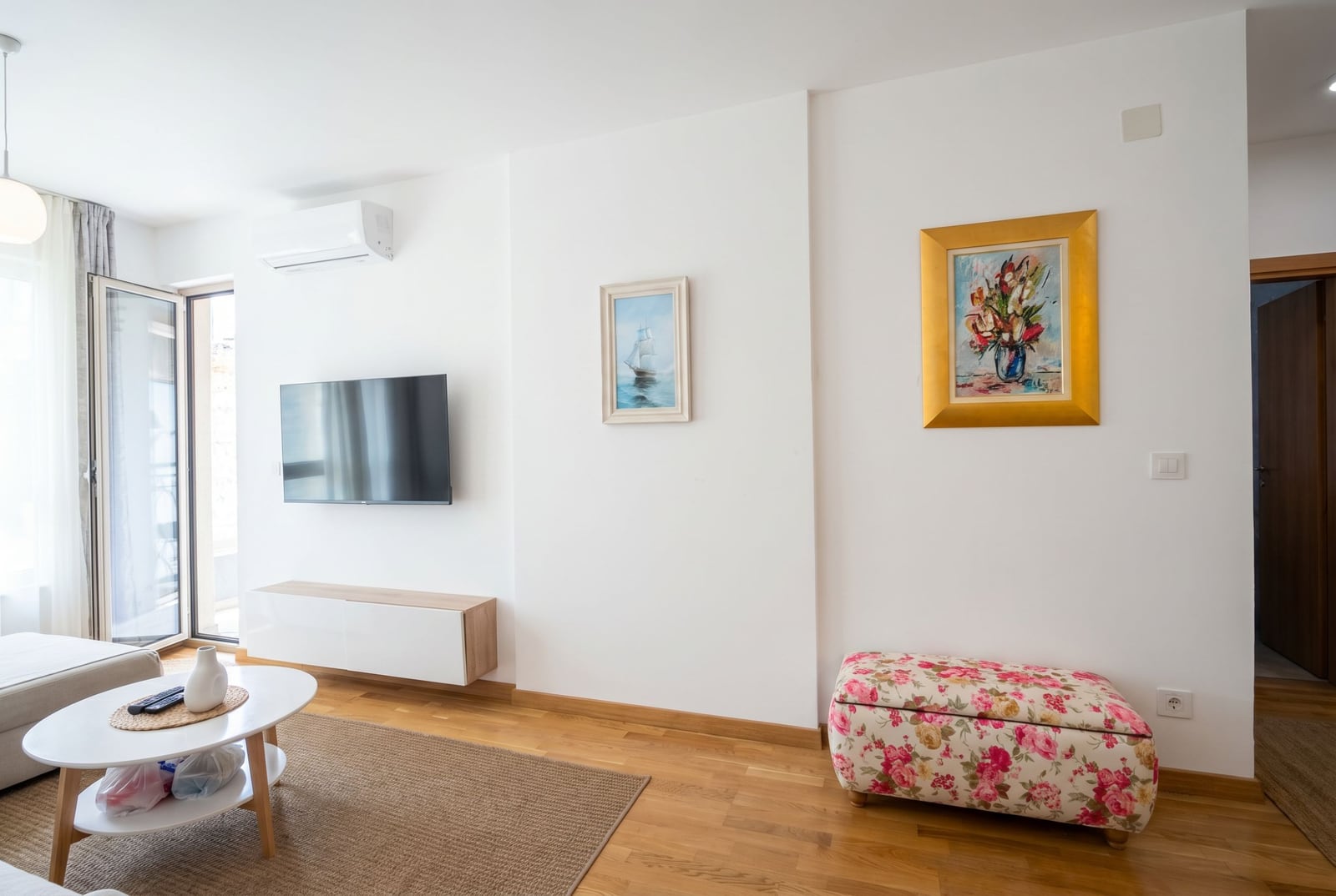 Bright living room in an apartment in Bečići, Montenegro: TV area, coffee table, parquet flooring, and access to the balcony.