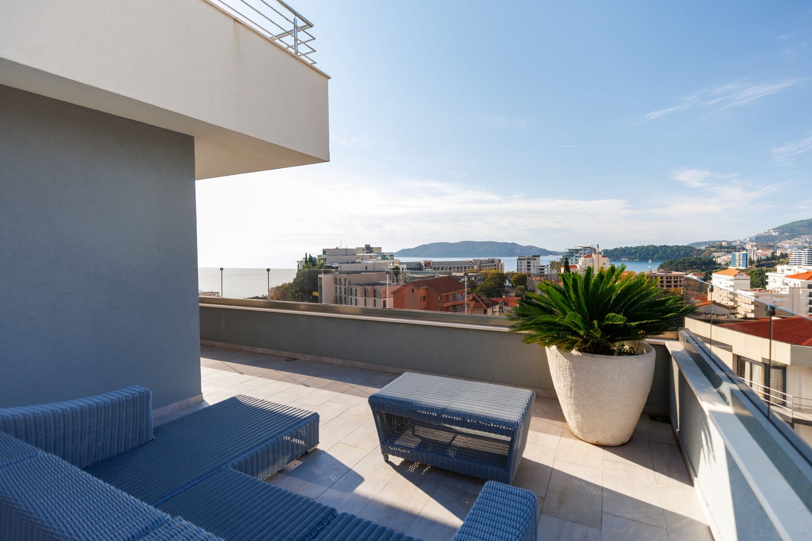 Spacious penthouse terrace in Becici, Montenegro, featuring wicker furniture and panoramic views of the sea and the city.