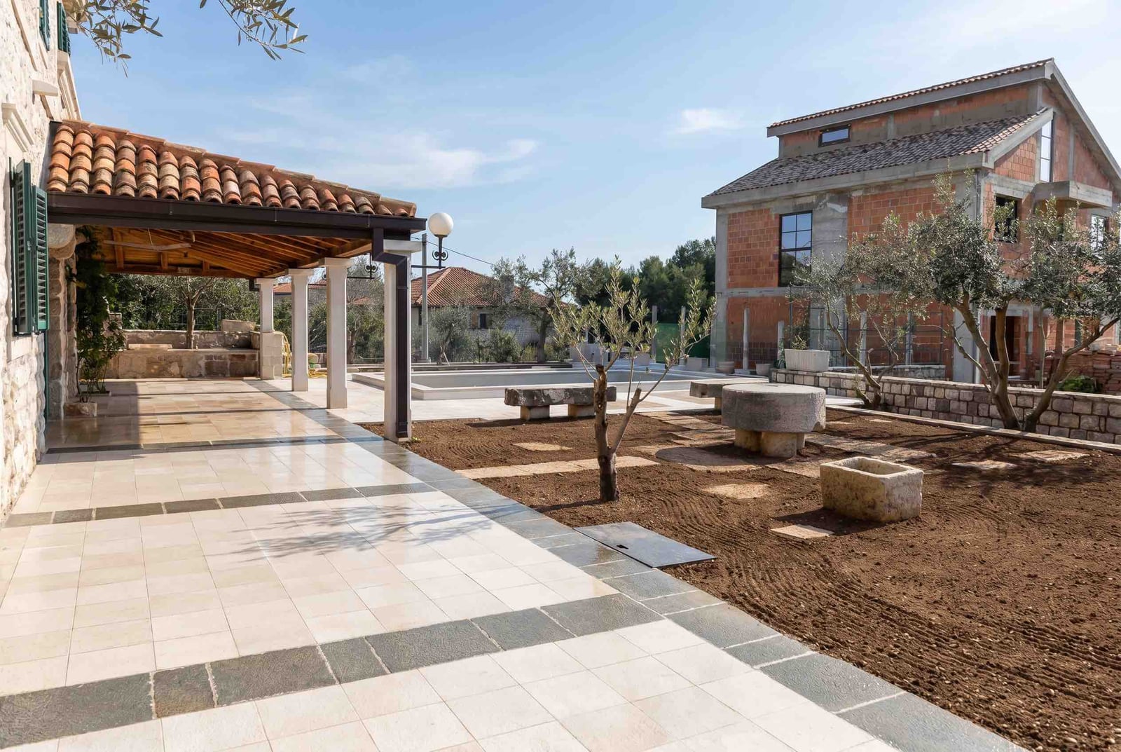 Stone-paved terrace, pool, and garden at a house in Luštica, Montenegro. View of the plot and the building under construction.