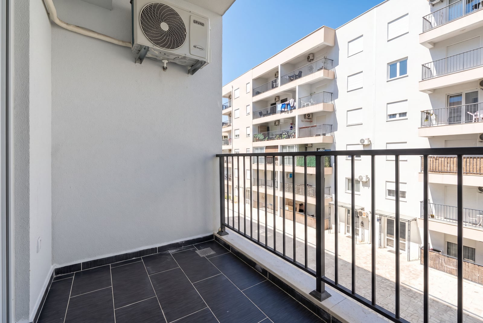 Empty balcony with black tiles and metal railing overlooking a residential apartment complex.