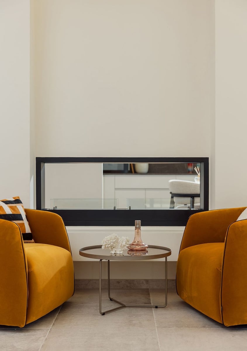 Modern living room with a fireplace and mustard-colored armchairs at a villa in Luštica, Montenegro: stylish interior with decor.