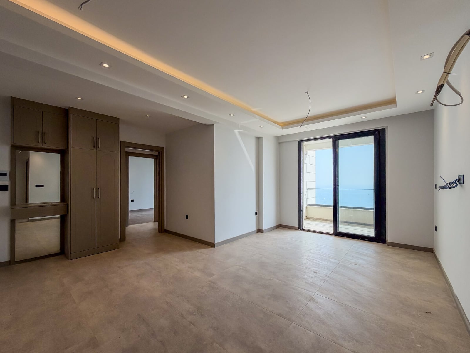 Empty room with built-in wardrobe and mirror, tiled floor, sliding door leading to a balcony overlooking the sea.