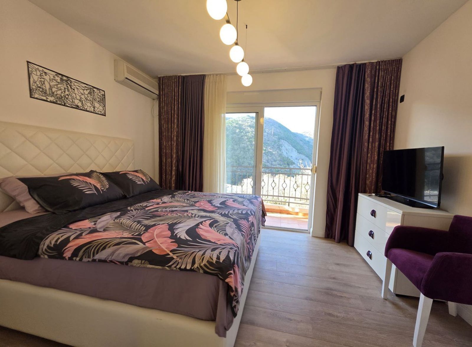 Bedroom in an apartment in Becici, Montenegro: double bed, TV, dresser, and a balcony with mountain views.