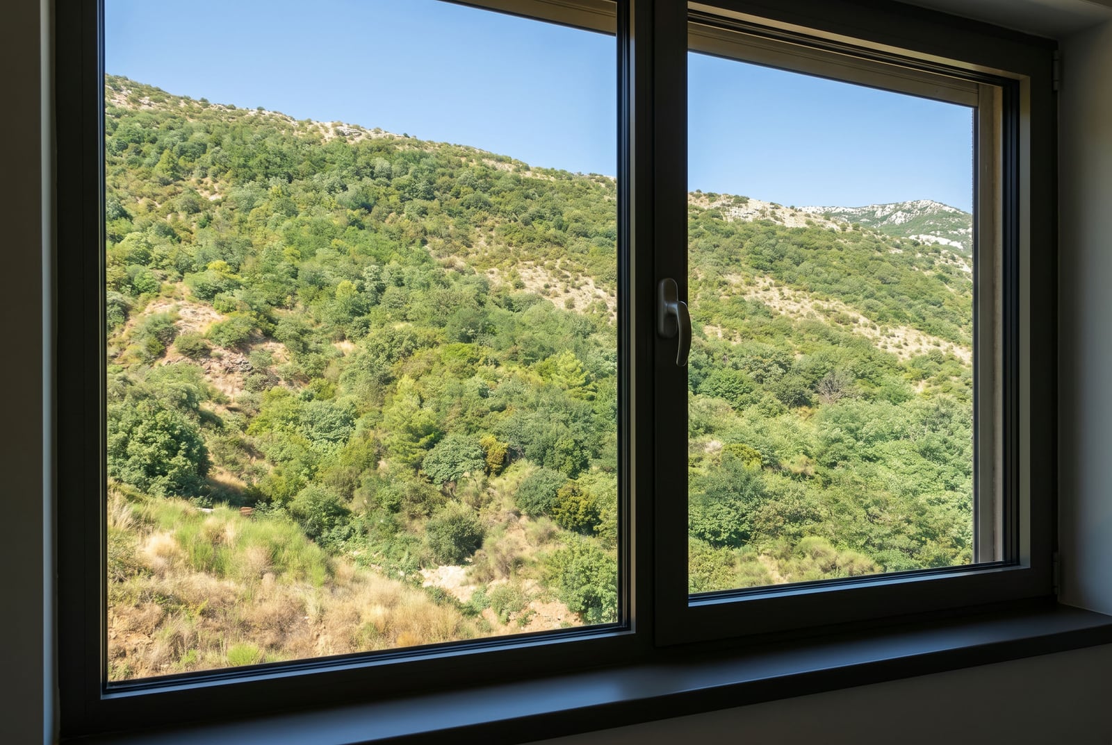View from the apartment window in Bečići, Montenegro: a panorama of green mountains and forested slopes seen through modern double-glazed windows.