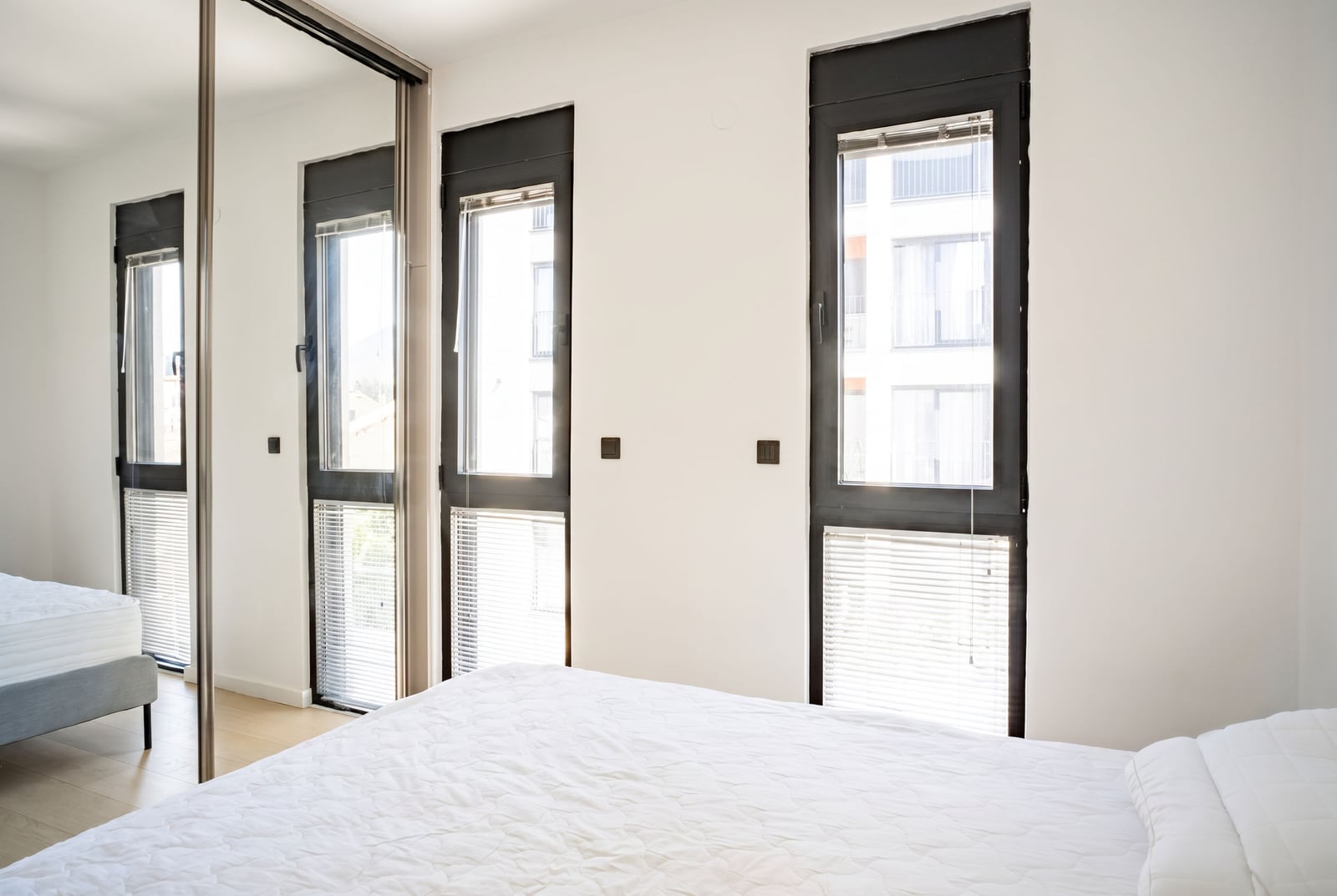 Bright bedroom with a large bed, panoramic windows, and a mirrored wardrobe in an apartment in Tivat, Montenegro.