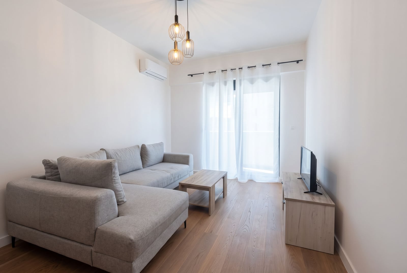 Bright room with a grey sofa, wooden coffee table, and TV on a light wood stand.