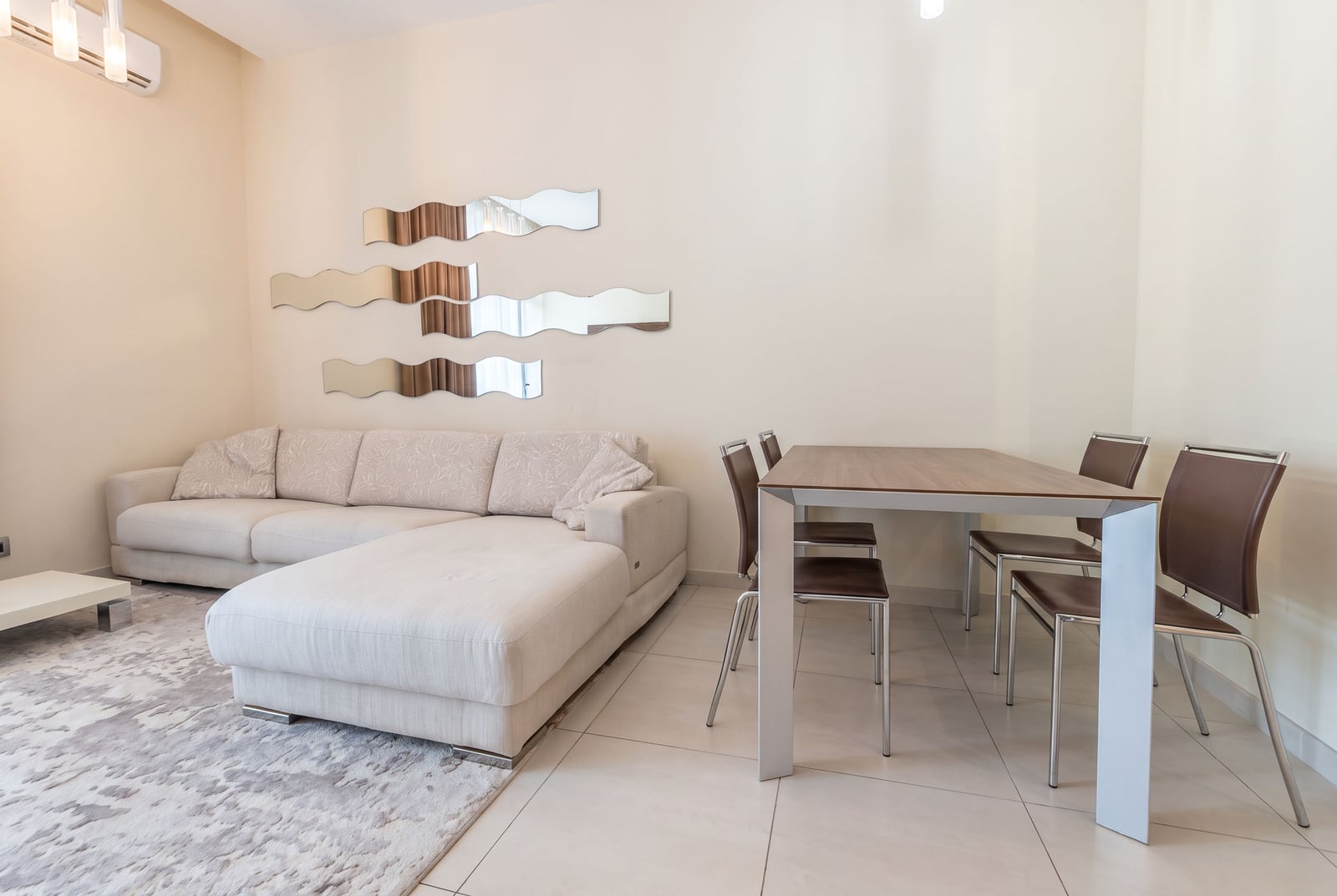 Bright room featuring a beige sectional sofa, dining table with chairs, and wavy mirror wall decor.
