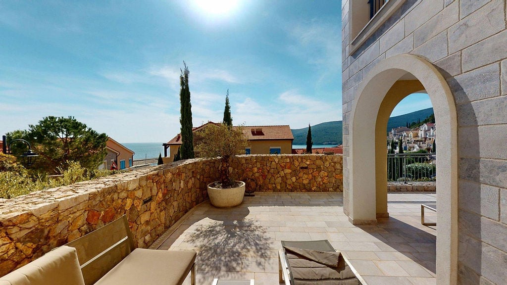 Stone-decorated terrace with sea views at the Luštica residential complex, Montenegro, featuring garden furniture and an archway.