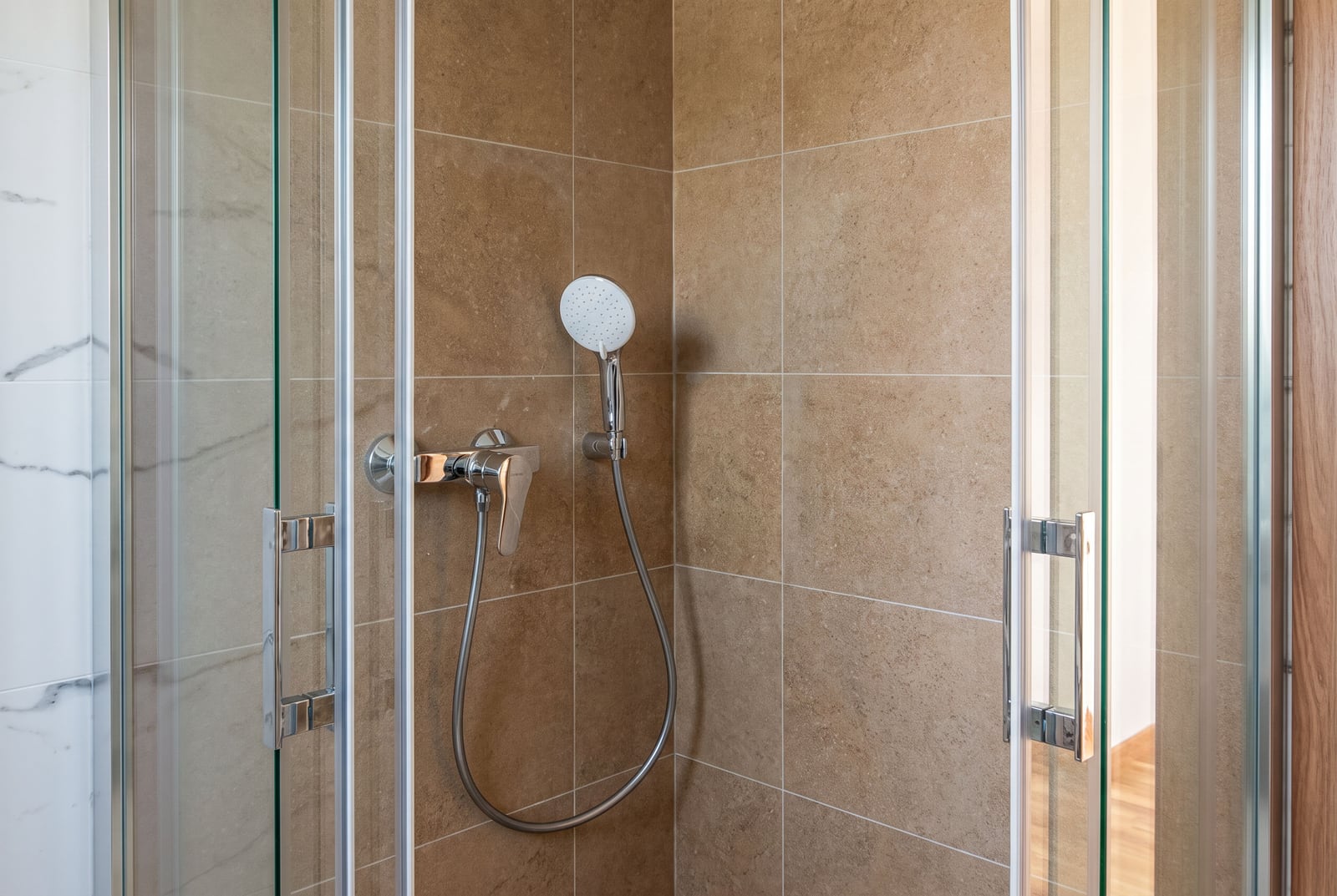 Modern shower cabin with beige tiles and a chrome faucet in an apartment, Budva, Montenegro