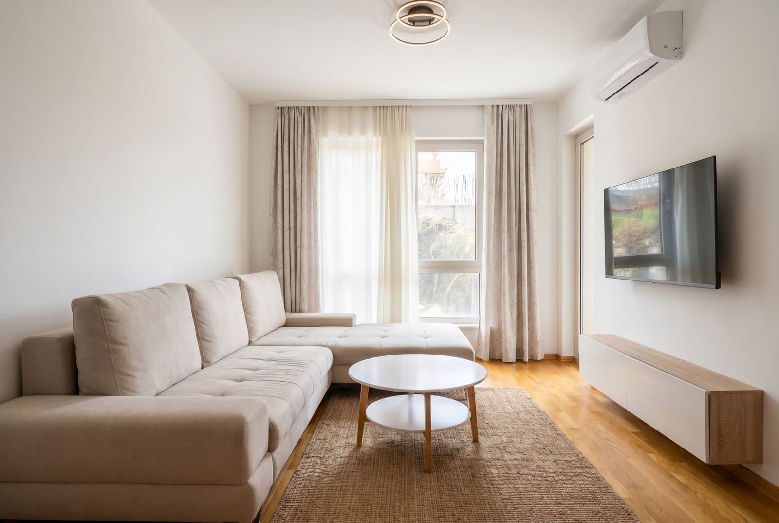 Modern living room with a beige sofa in an apartment in Bečići, Montenegro: bright interior, TV, and parquet flooring.